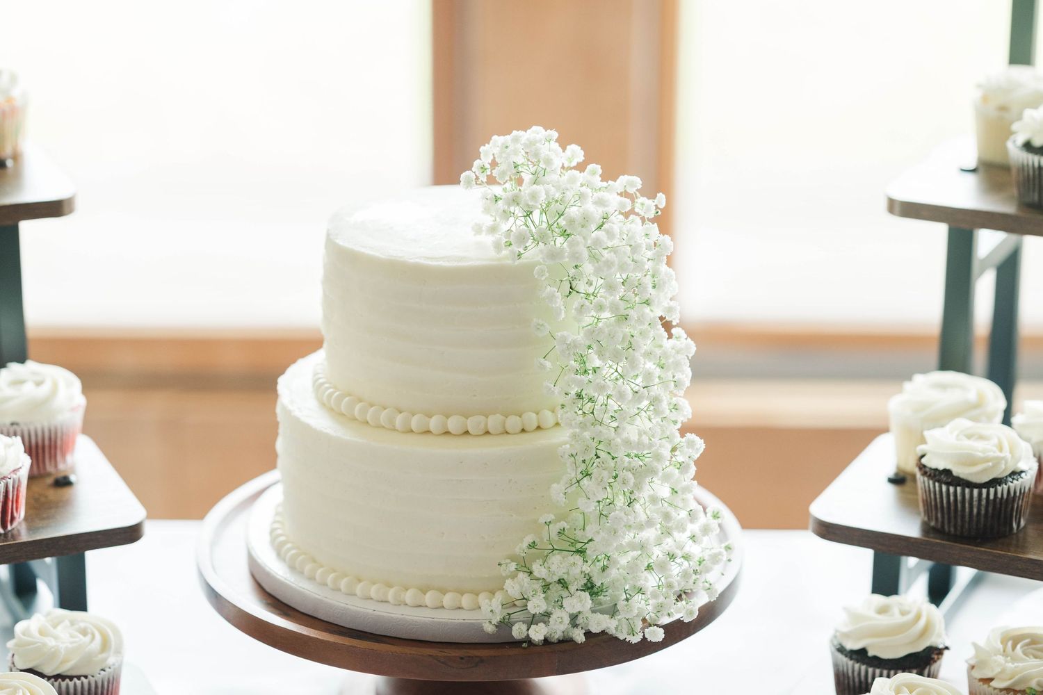 White wedding cakes decorated with delicate details and baby's breath flowers displayed on a dessert table.