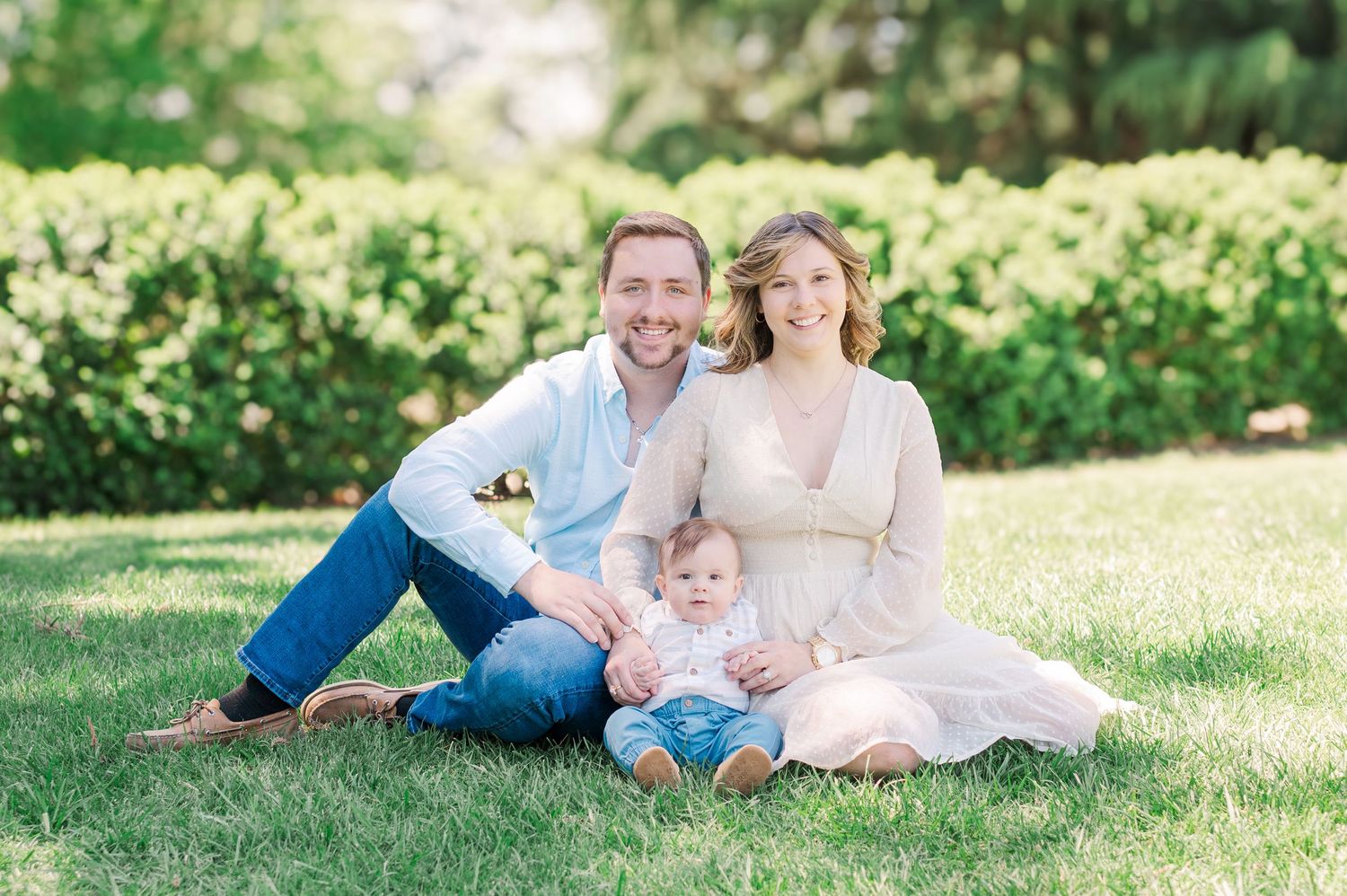 A family relaxes together on green grass during a sunny outdoor portrait session.