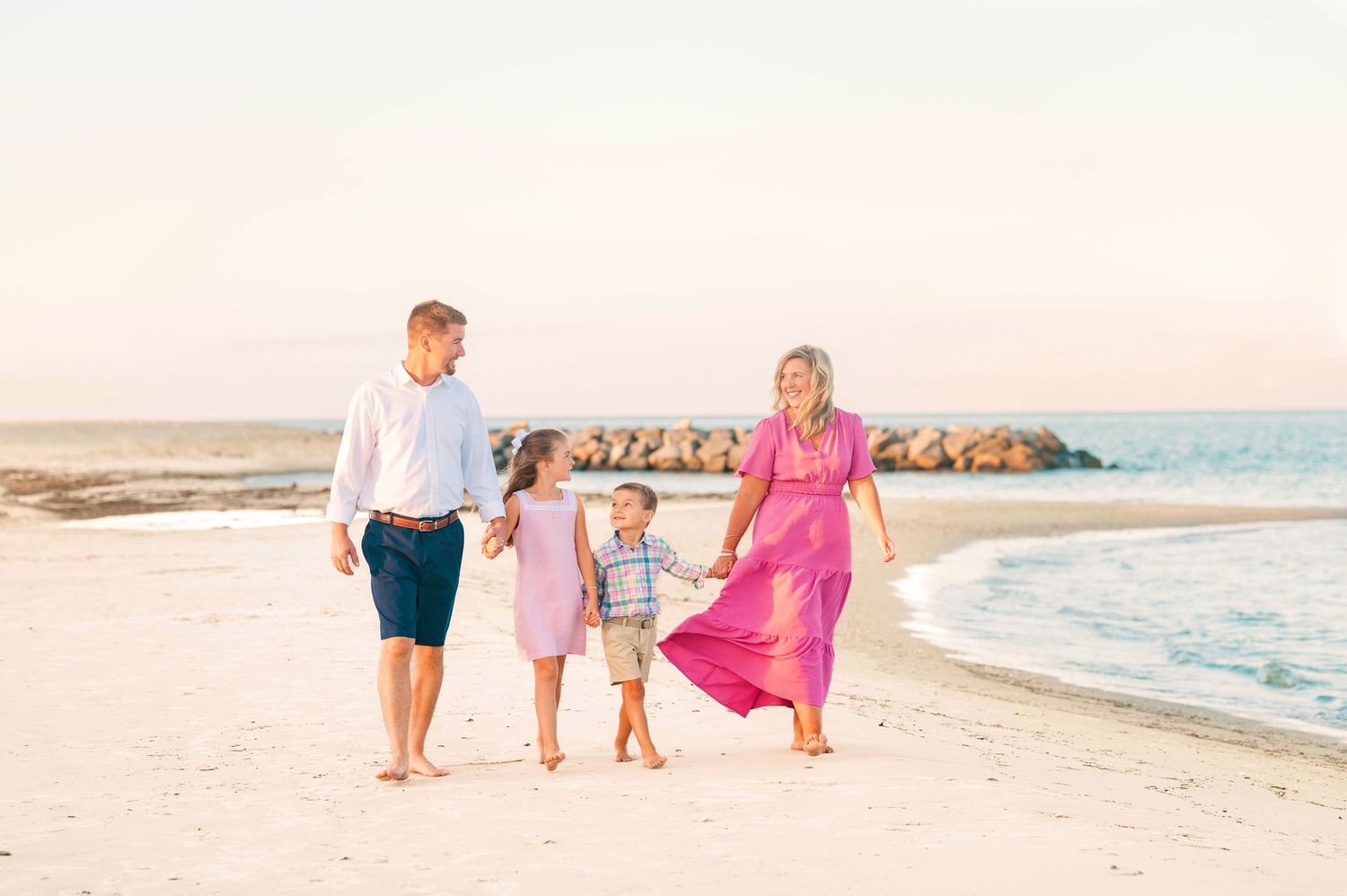 Family walking together along a sunset beach in pastel colored clothing.