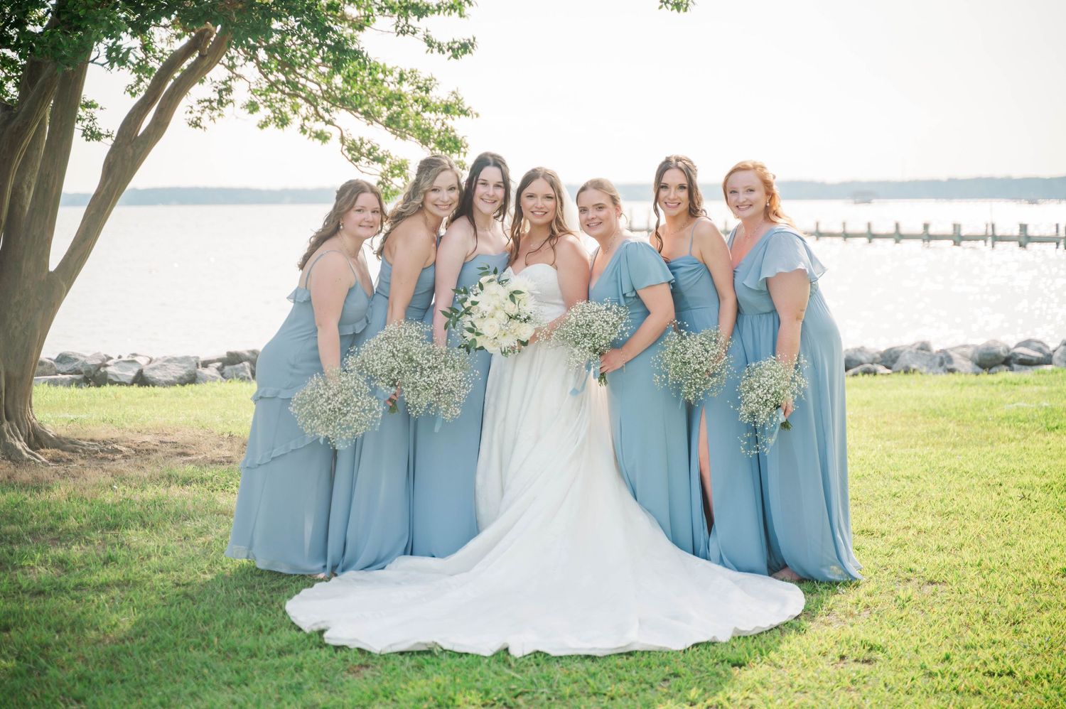Bridal party in powder blue dresses stands together for formal photos outdoors.