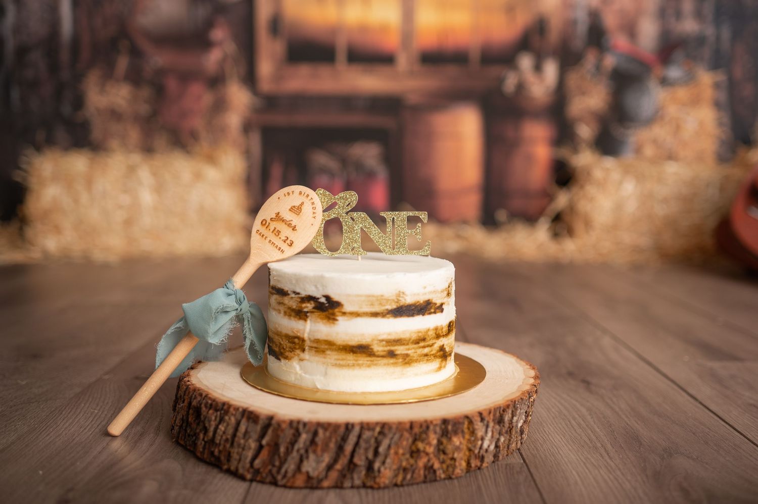 Rustic cake display on wooden slice with ONE topper against barn wood background.