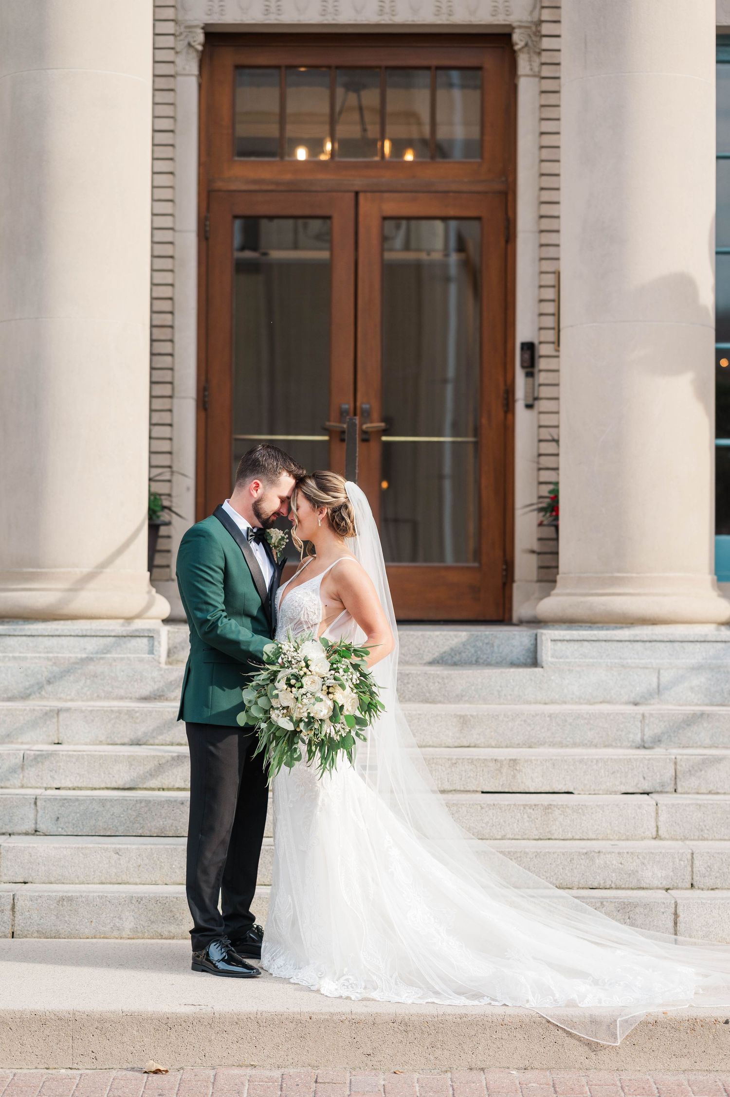 Elegant wedding portrait against classic brick architecture with white columns.