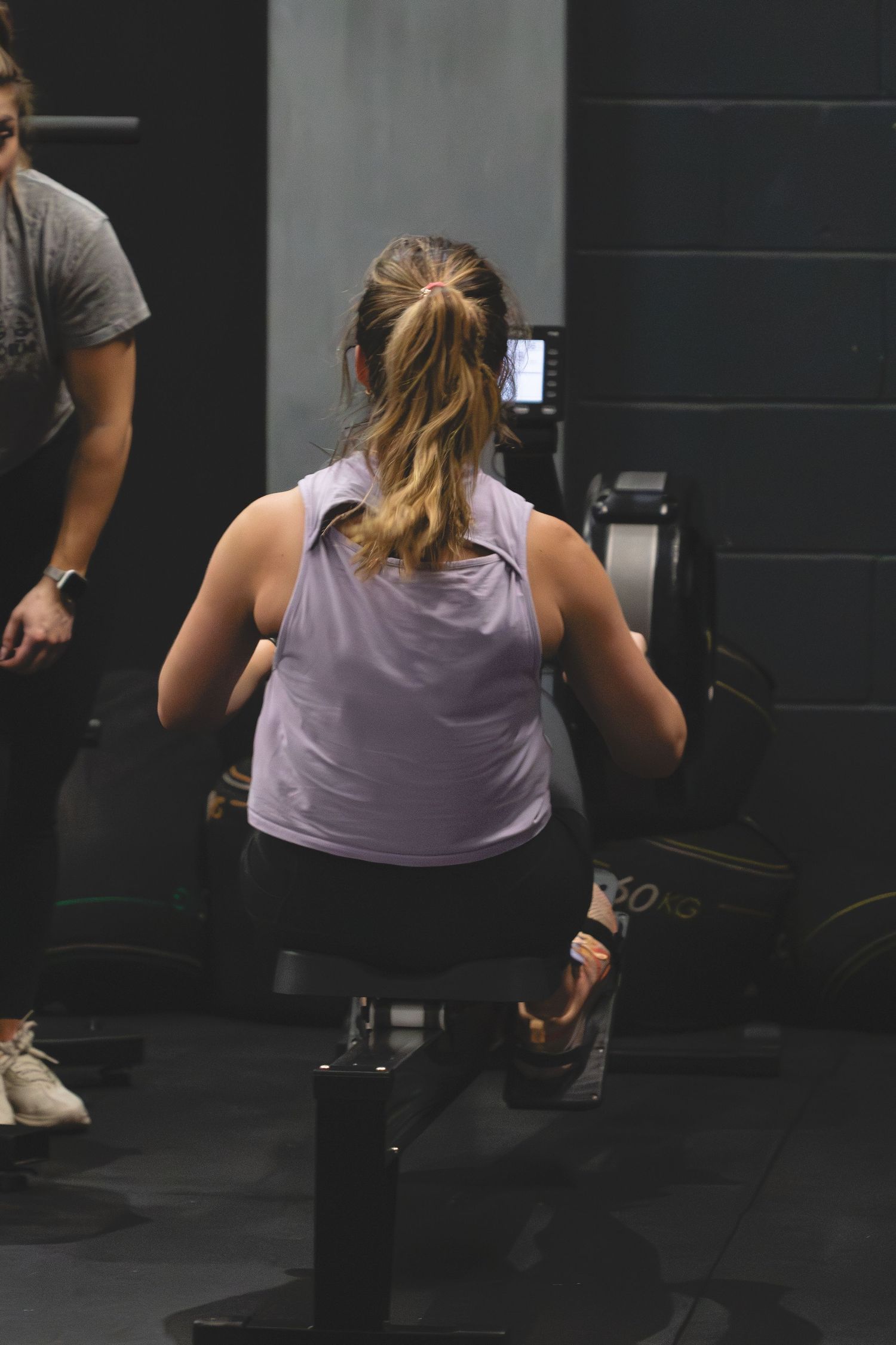 Person in purple tank top performing lunges during an indoor gym workout session.