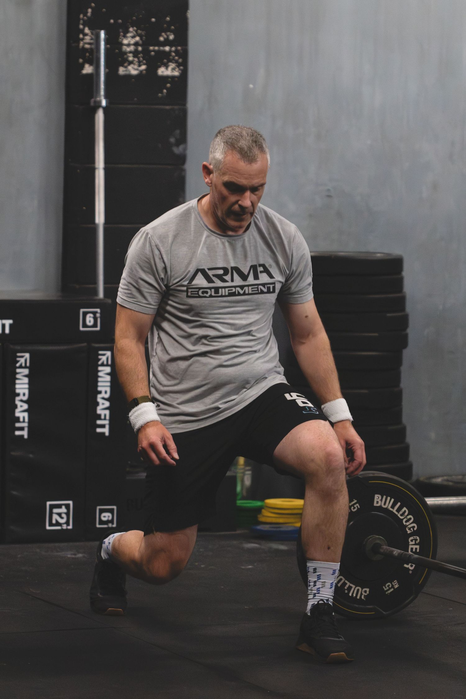 A person performing an exercise sequence in a gym wearing a gray t-shirt and black shorts.