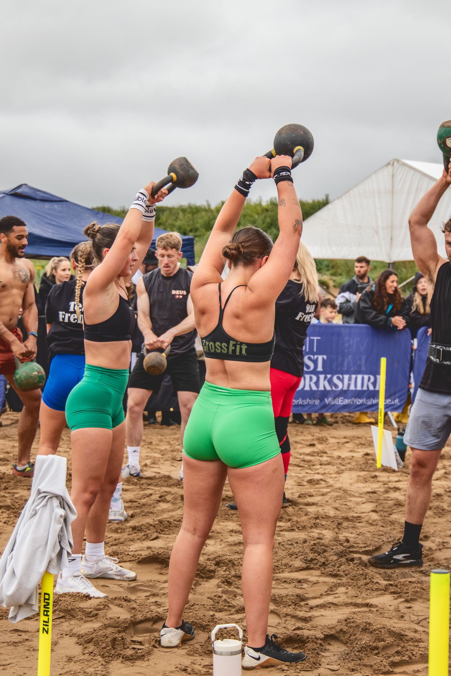 A line of CrossFit athletes performing kettlebell exercises on a sandy beach during an outdoor fitness competition.