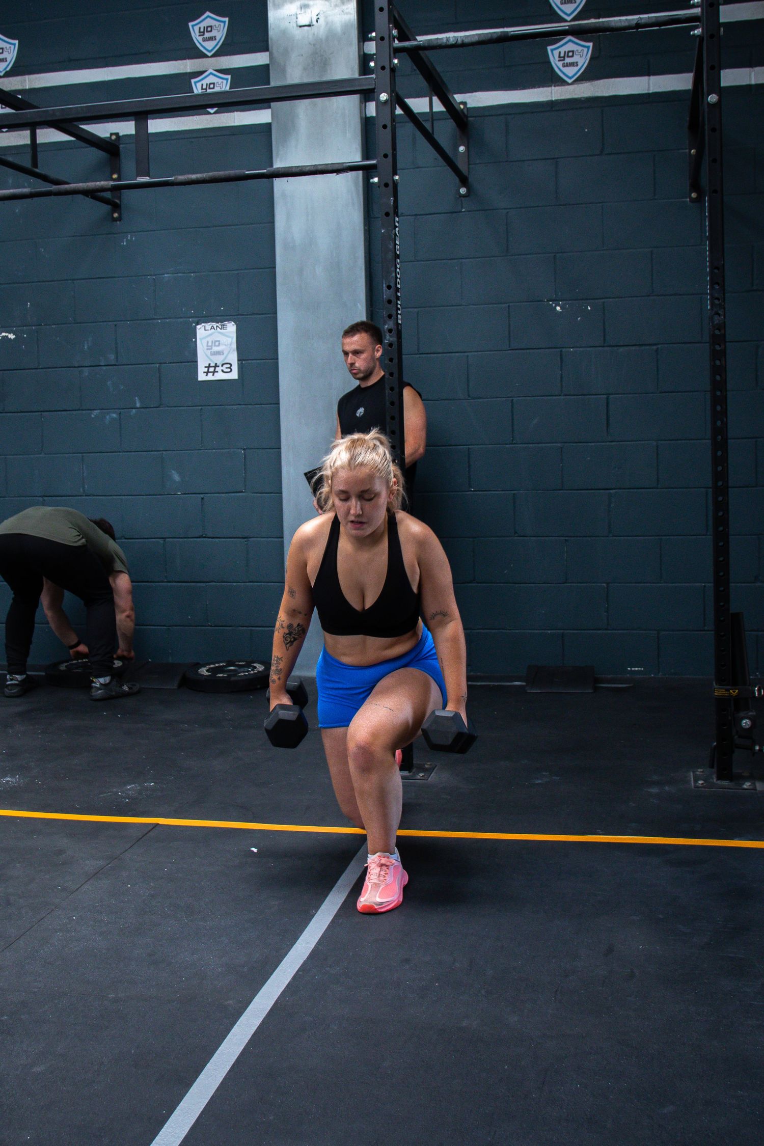 Athletes perform lunges in sequence during a CrossFit workout at a gym with blue walls and yellow floor markings.