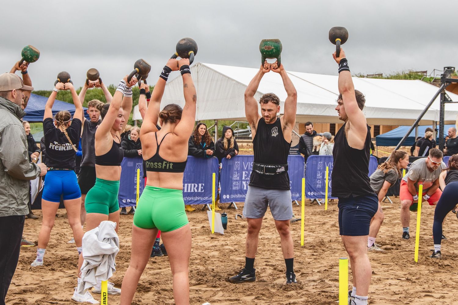 Athletes perform synchronized kettlebell workouts on a sandy beach during an outdoor fitness competition event.