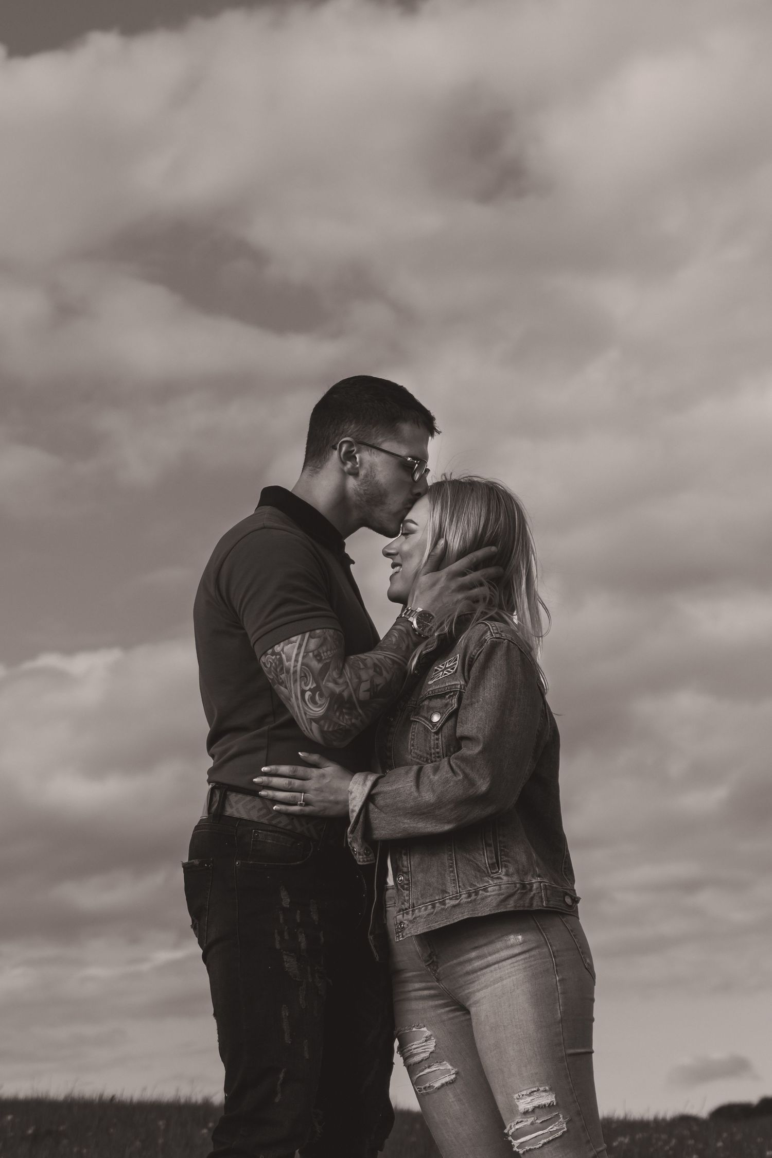 Intimate black and white portrait of a couple embracing in a field.