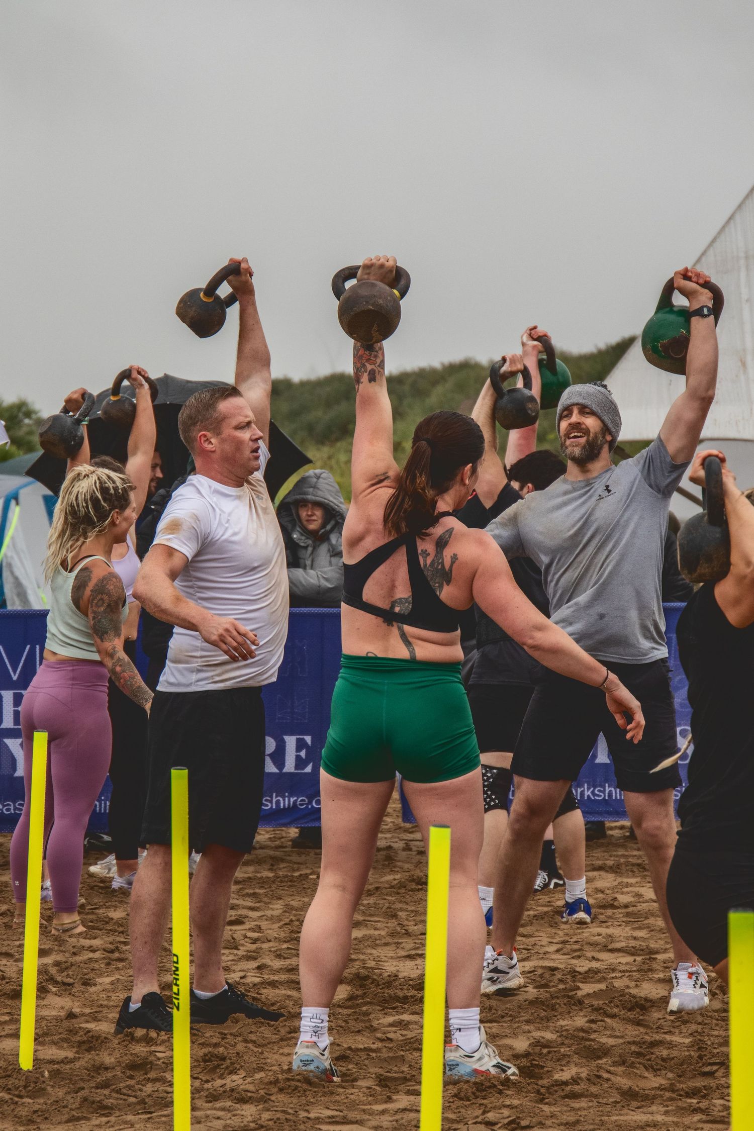 Fitness group exercising together outdoors doing kettlebell swings in a synchronized formation during a workout class.