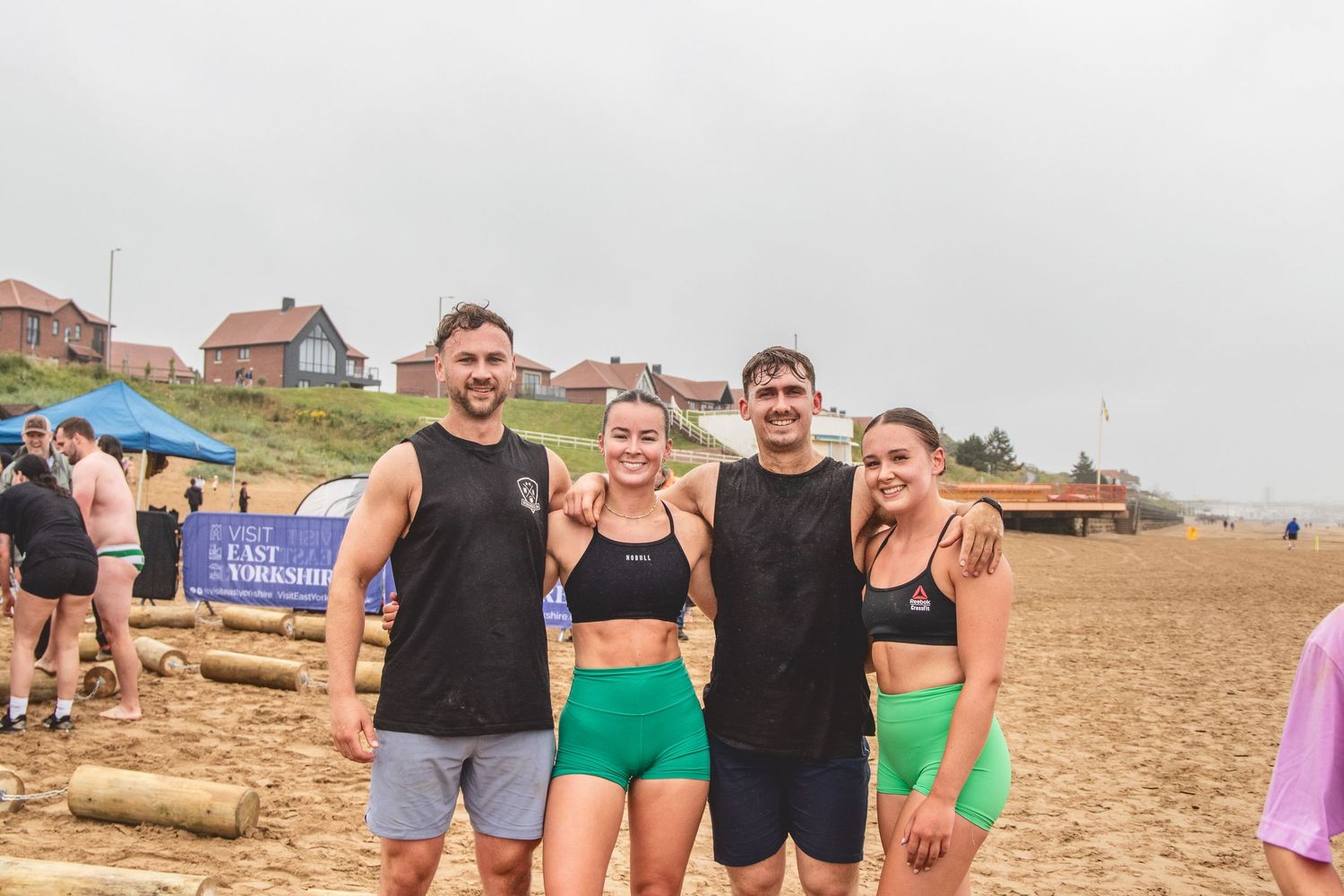 A group enjoys a beautiful summer day at a sandy beach with dunes and houses in the background.