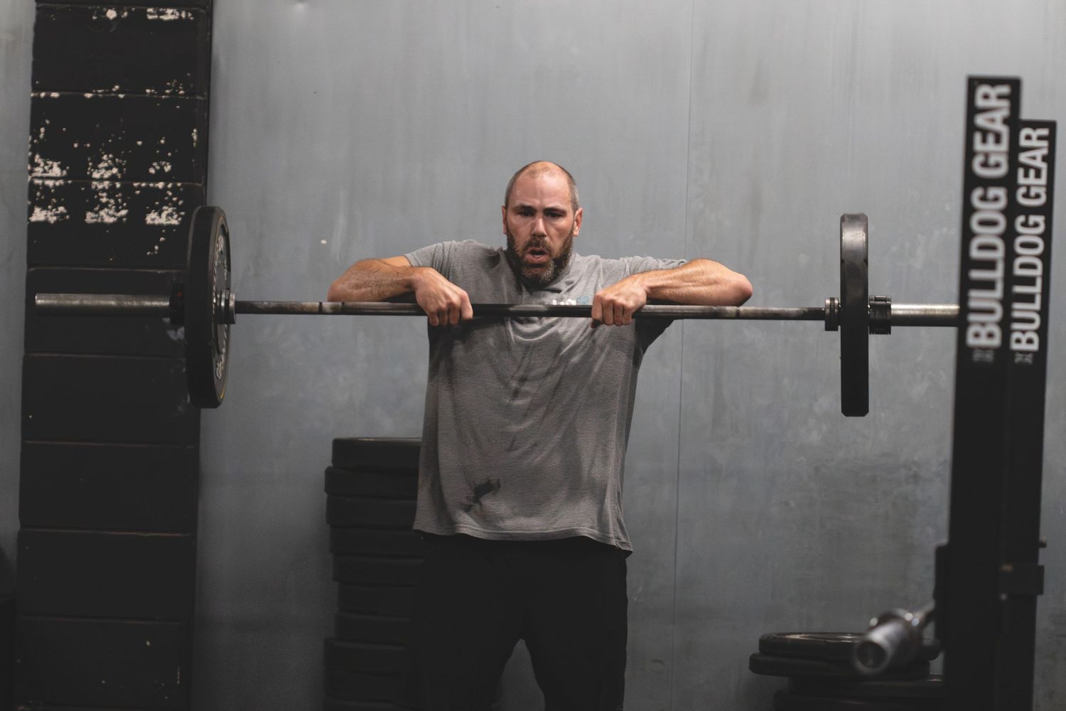 Person holding a barbell in a front rack position during weightlifting session at a dark gym.