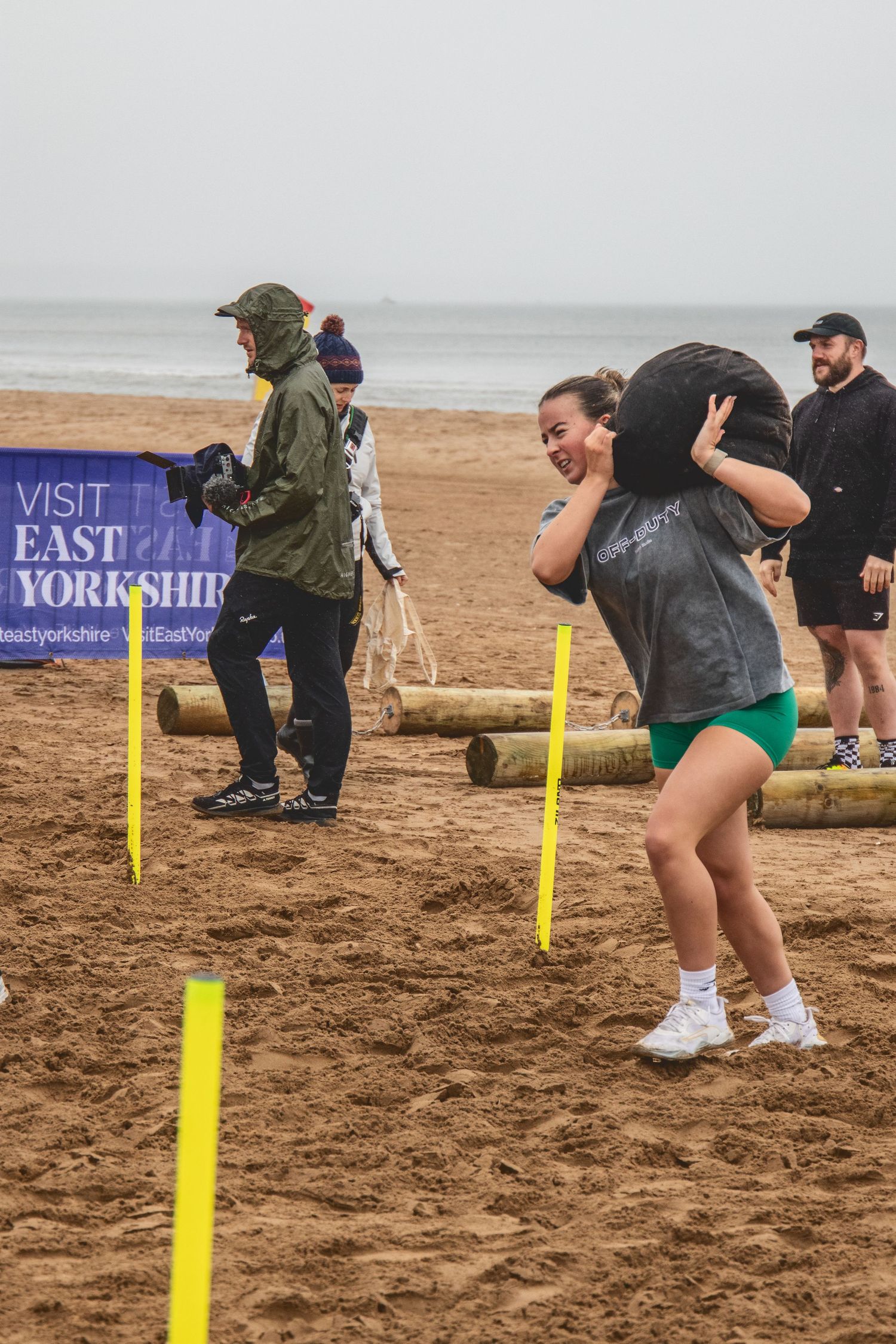 People participate in a beach fitness event in East Yorkshire on a cloudy day with yellow course markers in the sand.