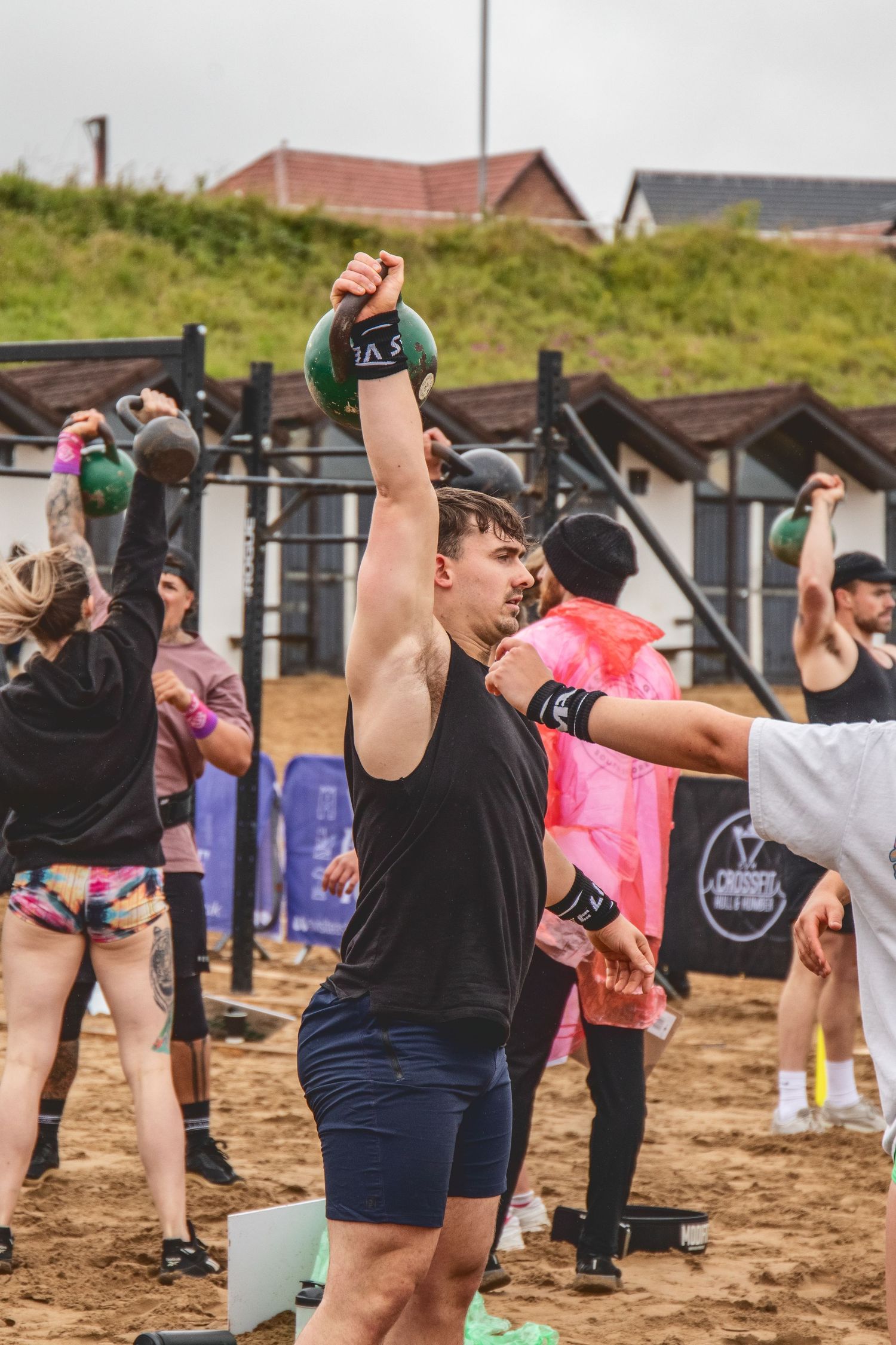 A group of fitness enthusiasts perform outdoor kettlebell exercises on a beach during a workout class.
