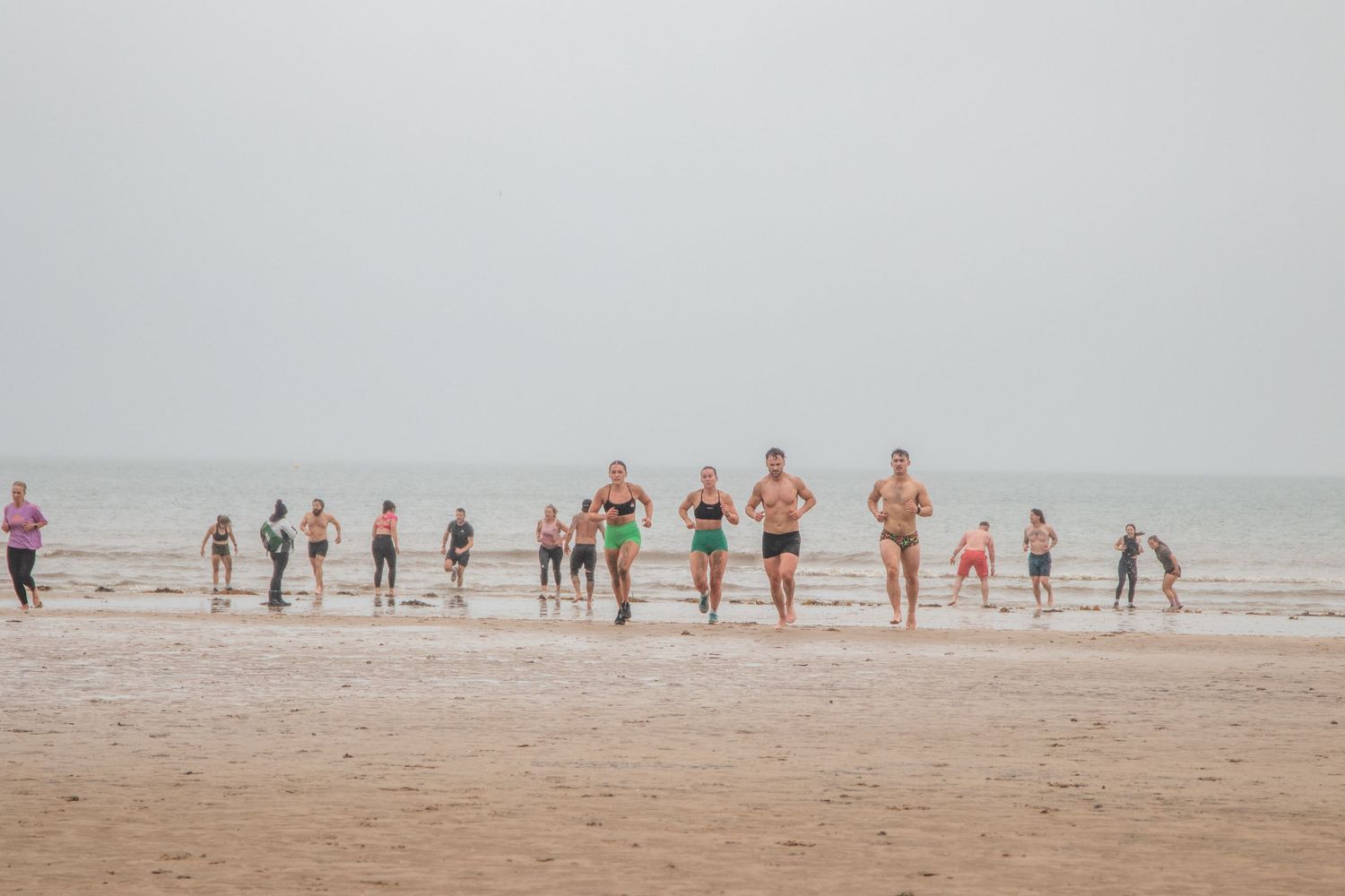 People exercising and warming up on a foggy beach during a morning workout session.