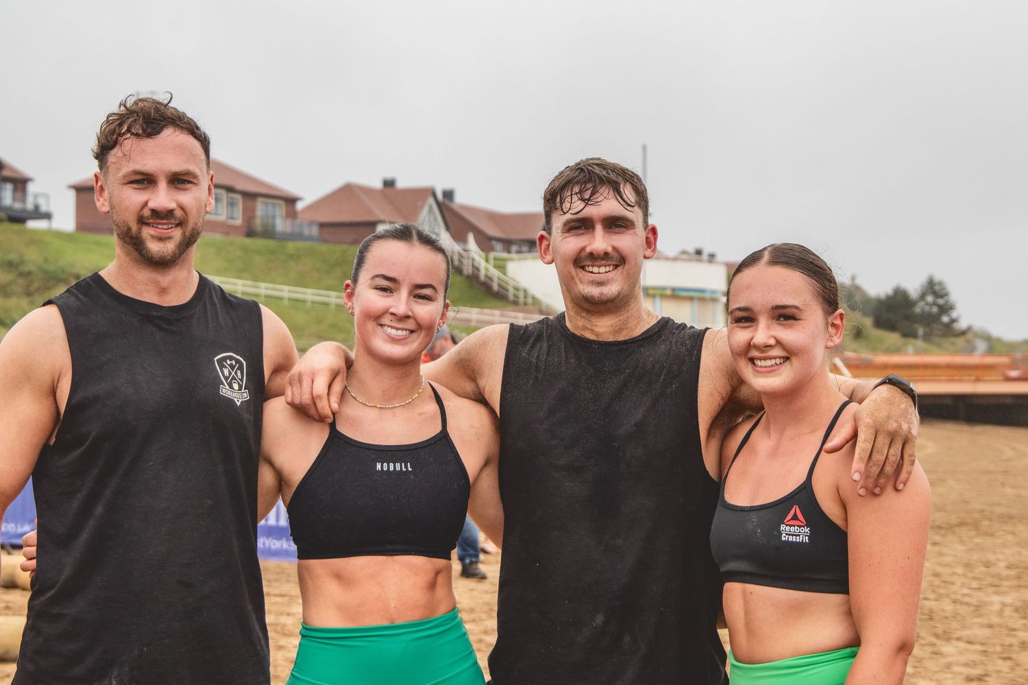 A group of four athletic people in workout attire standing together and smiling outdoors.