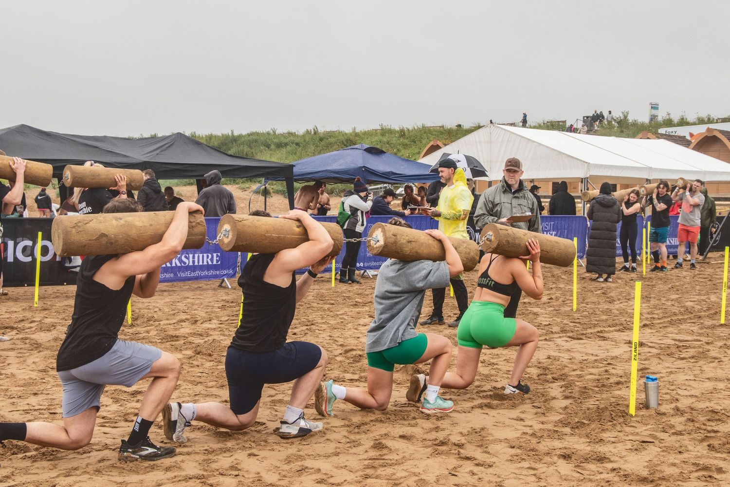 Group of athletes performing synchronized squats on sandy beach during outdoor fitness competition or event.