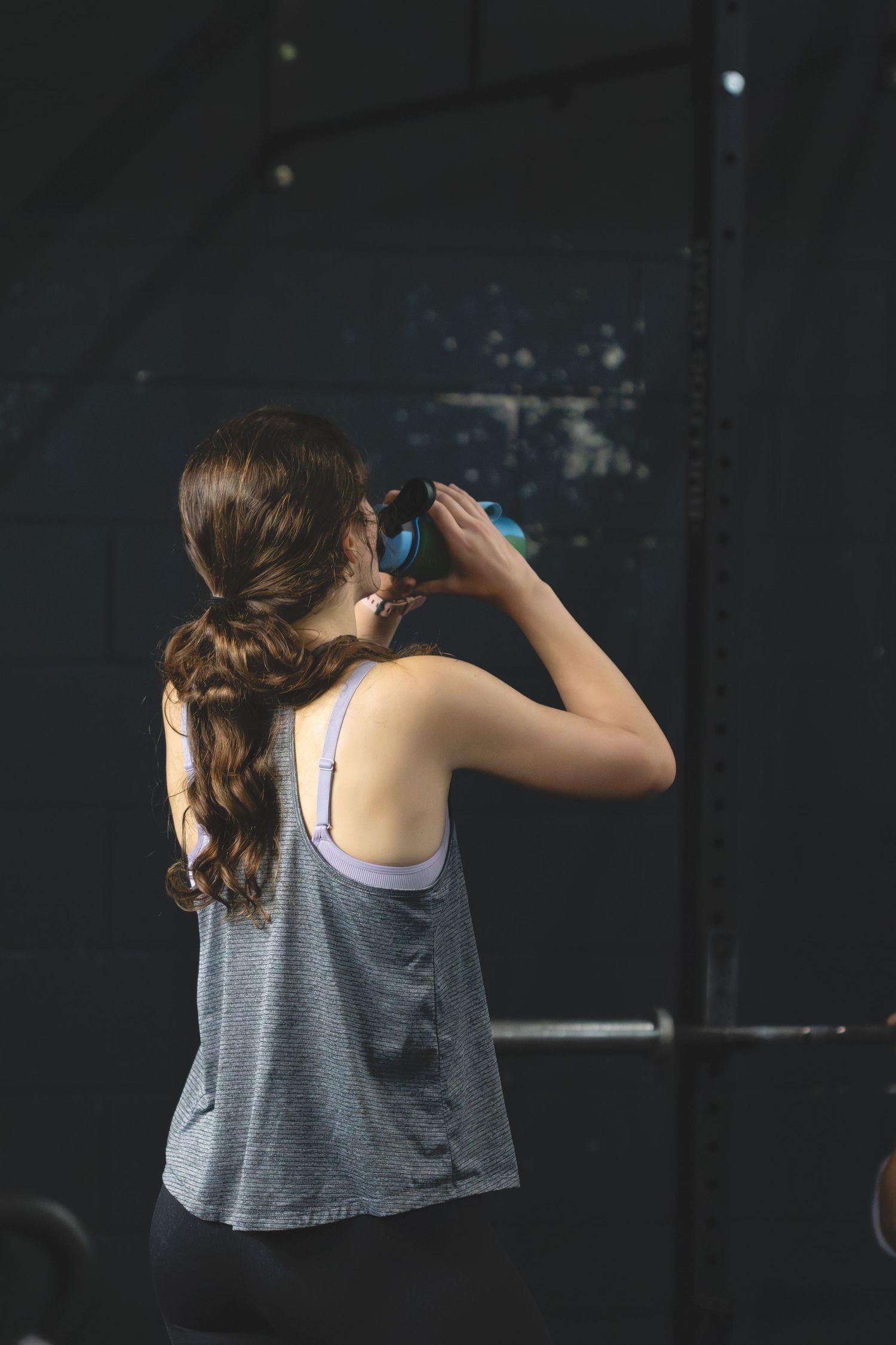 Person in a gray tank top drinks from a blue water bottle during what appears to be a workout session.
