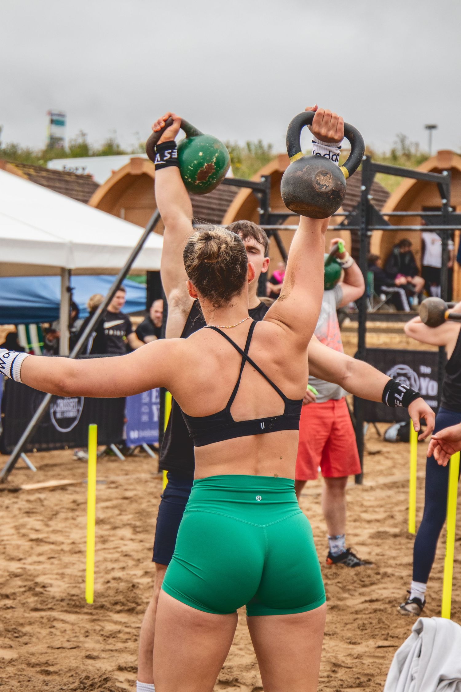 Athletes performing overhead plate exercises on a sandy beach during a fitness competition.