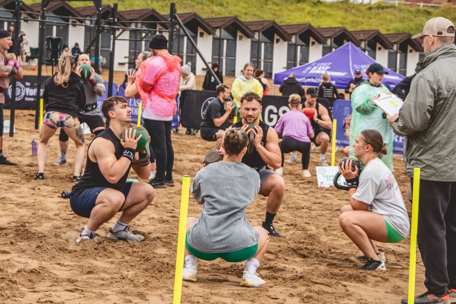 Athletes perform synchronized squats during an outdoor group fitness class on muddy terrain.