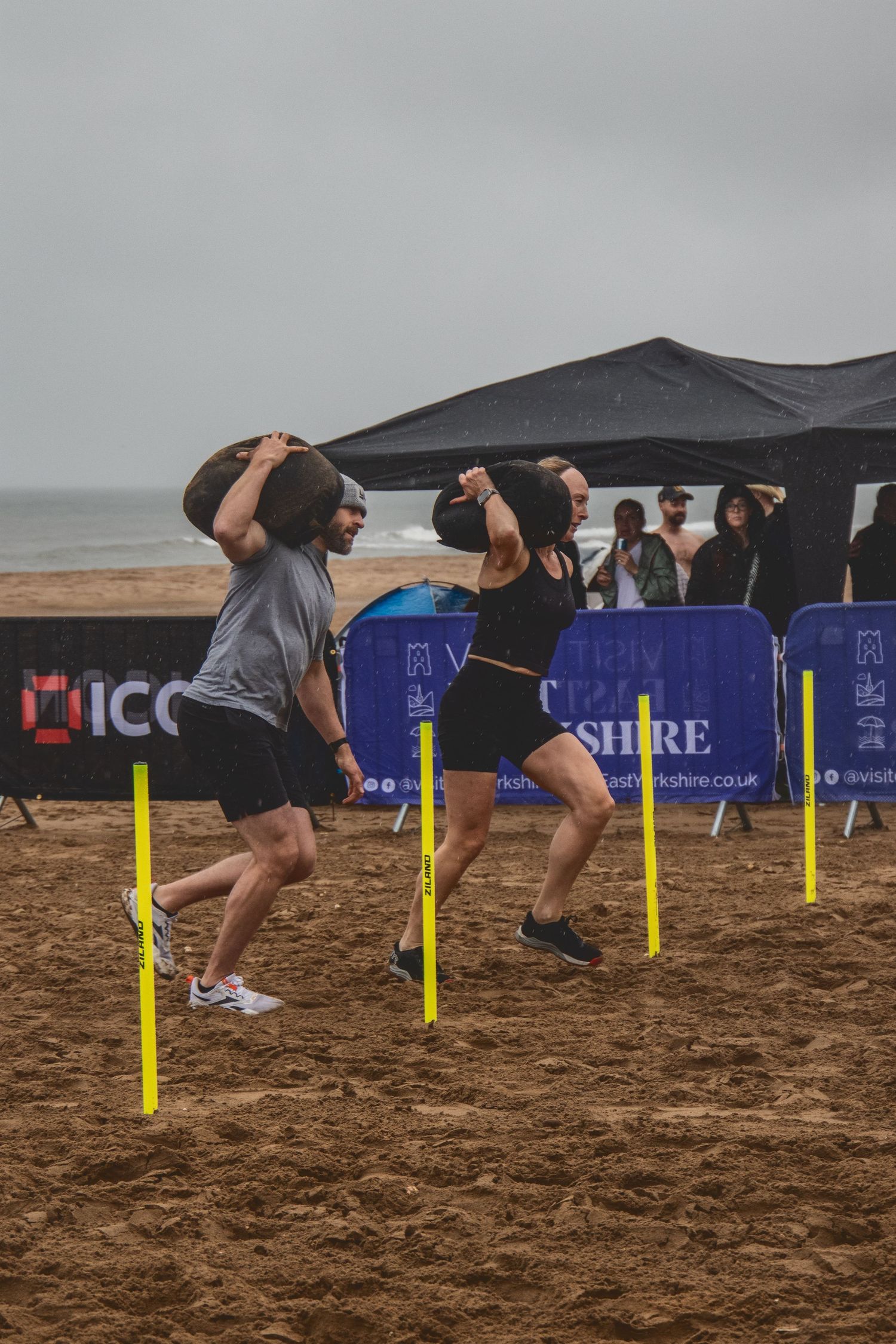 A sequence of action shots showing someone hurdling over yellow poles in the sand during an athletic training exercise.