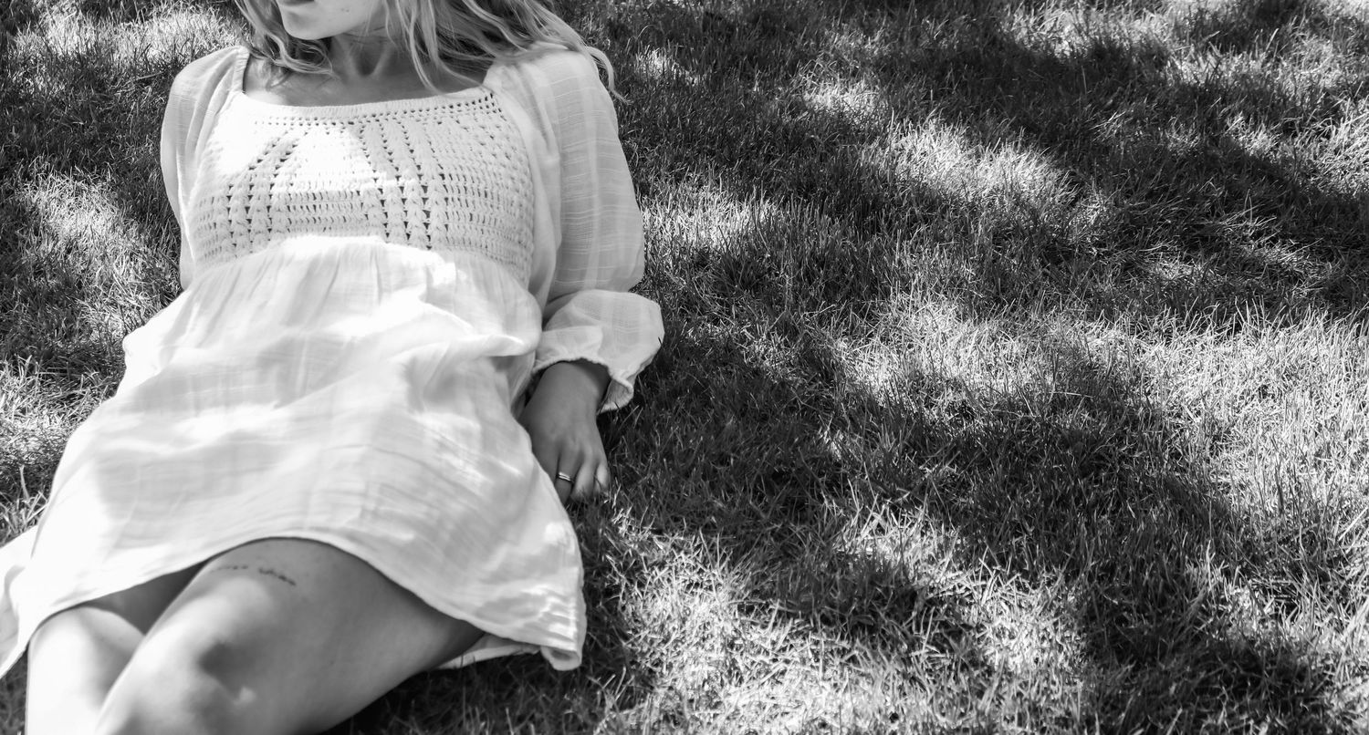 Black and white portrait of person wearing white dress relaxing on grass.