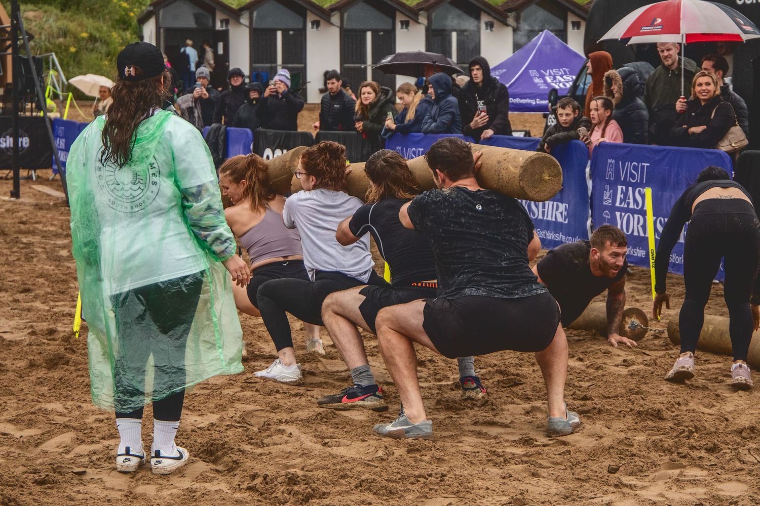 Team of participants preparing to pull in a beach tug-of-war competition while spectators watch with umbrellas.
