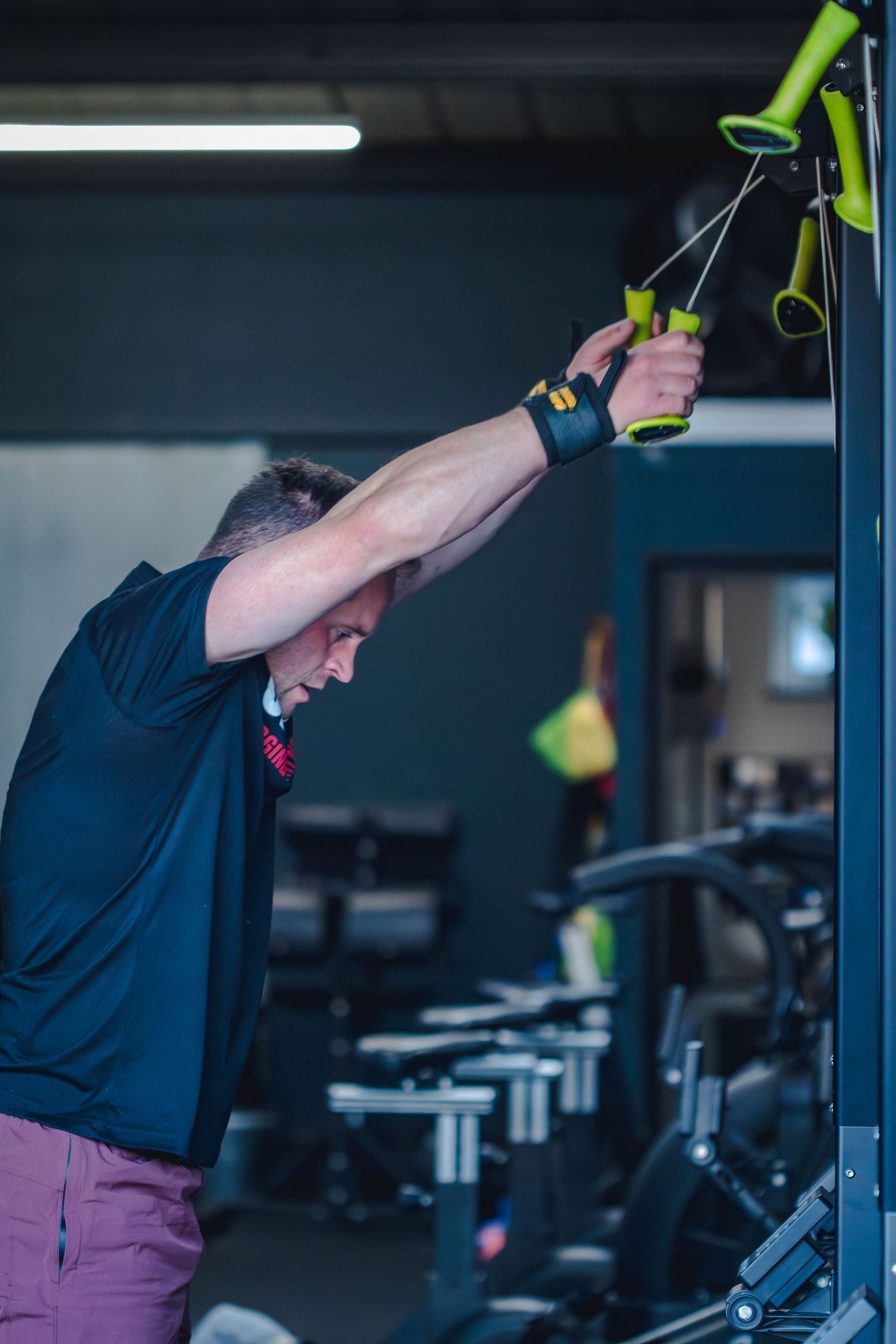 Person performs tricep pushdowns using green resistance straps in a dark gym setting.
