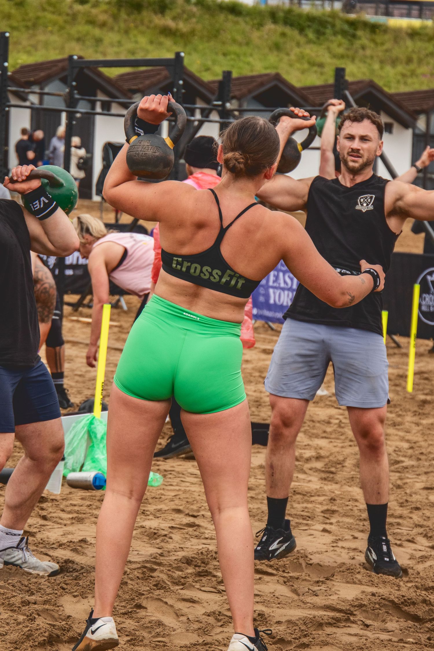 Fitness enthusiasts participate in an outdoor CrossFit training session on a sandy beach area wearing athletic gear.