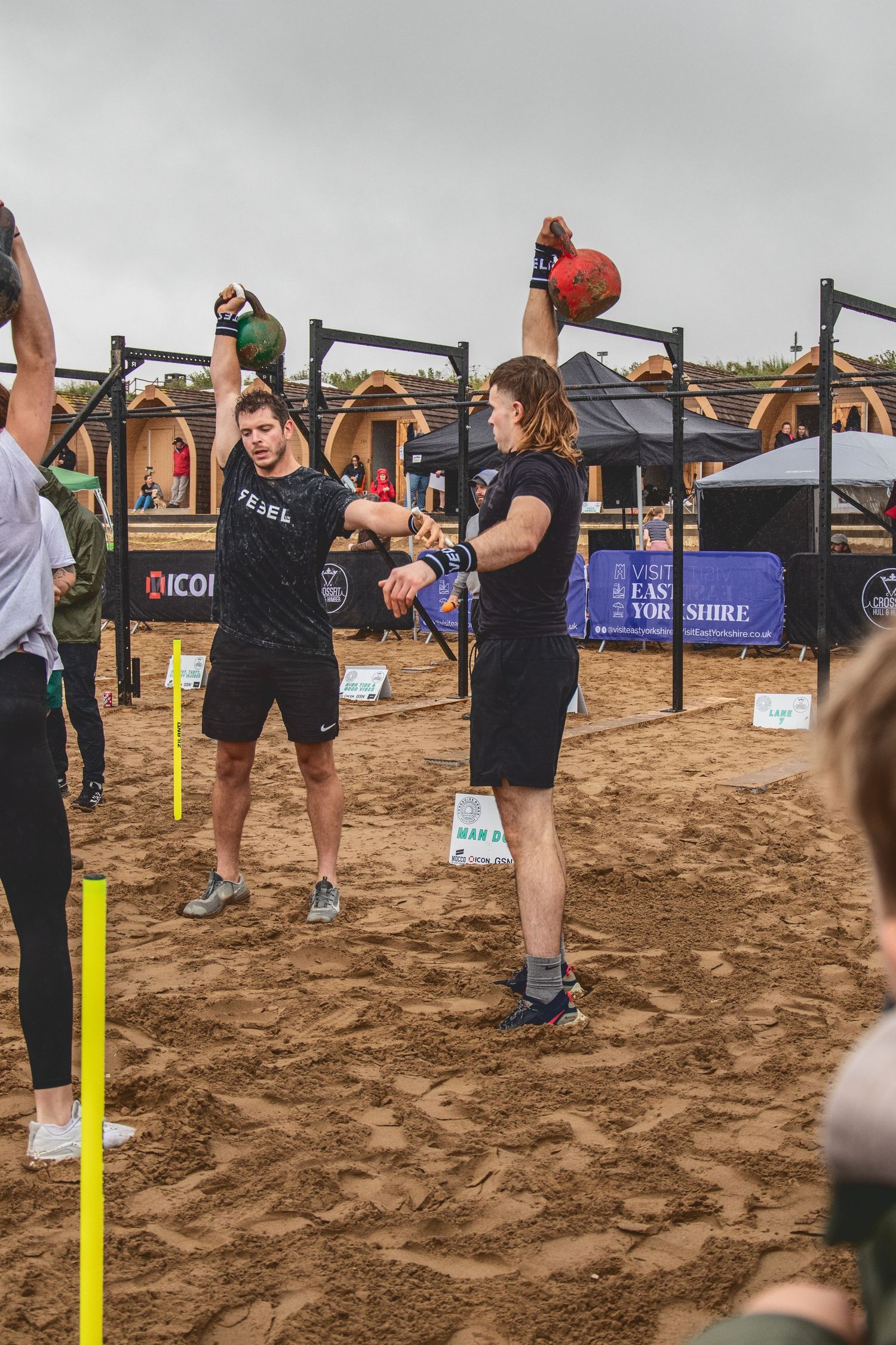 Athletes training outdoors with kettlebells on sandy ground at a fitness competition or workout event.