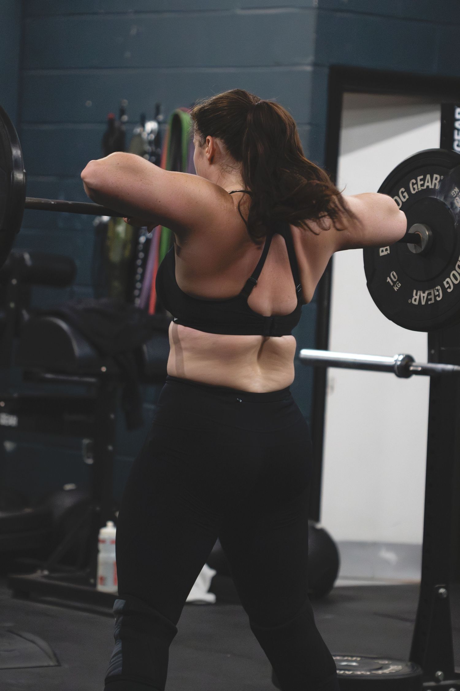 Person performing barbell squats in black athletic wear at a gym focusing on proper form and technique.