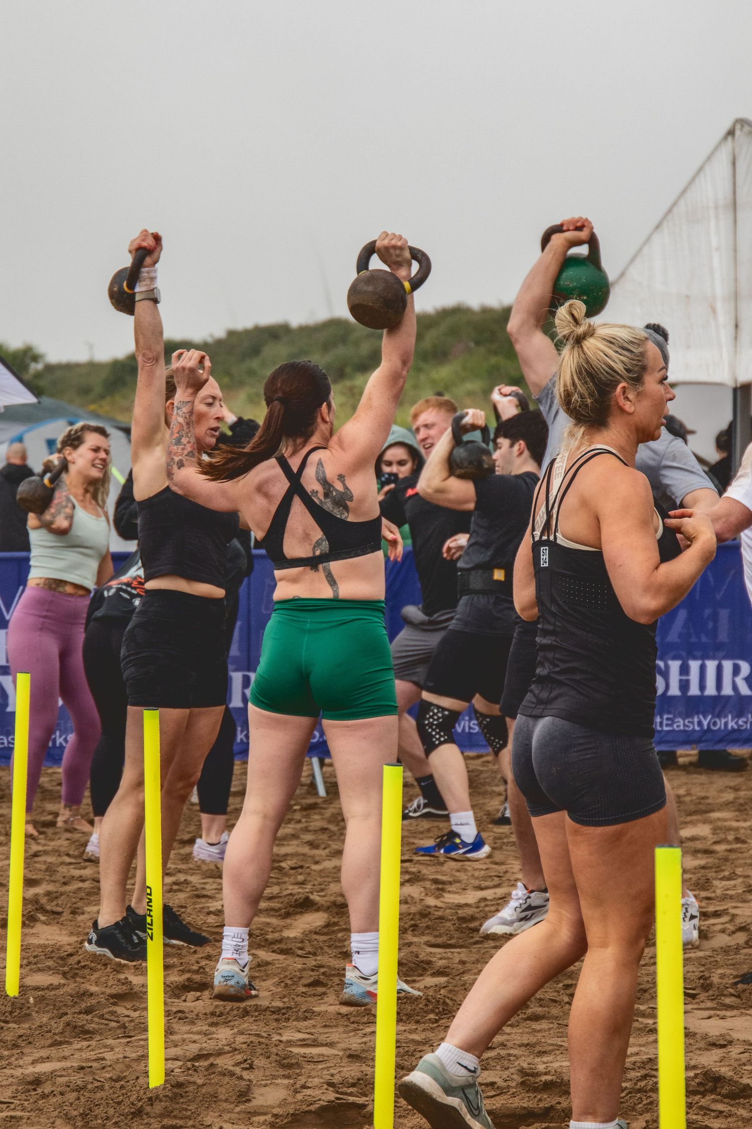 Group of athletes performing exercises with kettle bells on a sandy beach during an outdoor fitness class.