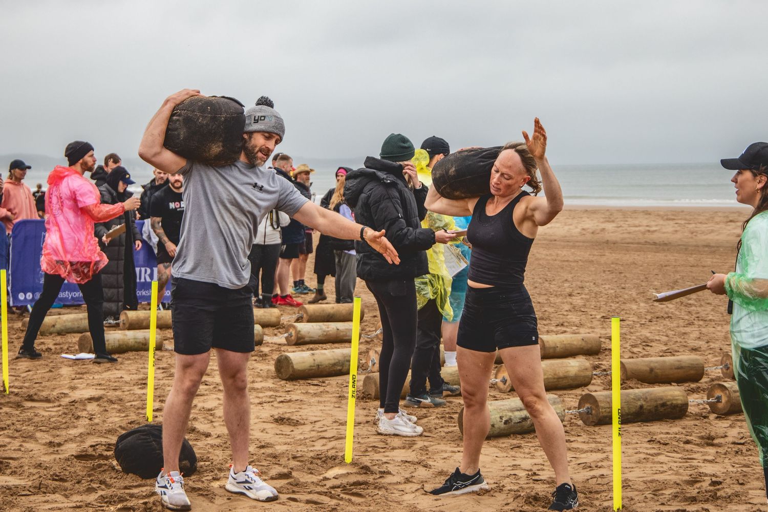 Group of people exercising on a beach with yellow poles during an outdoor fitness class by the ocean.