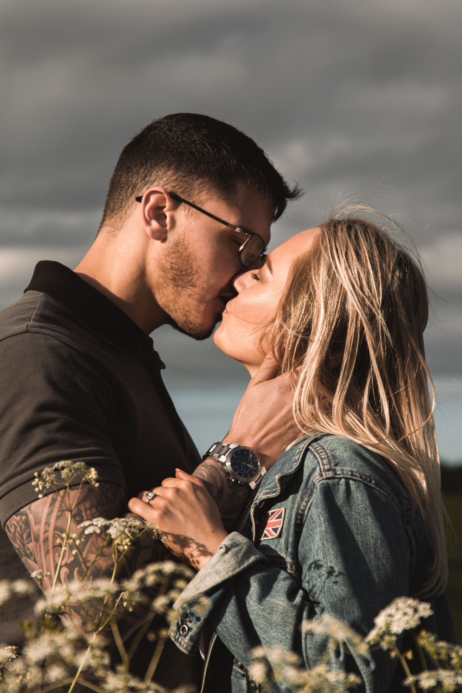Side view of couple's tender kiss amid blooming meadow under moody sky.