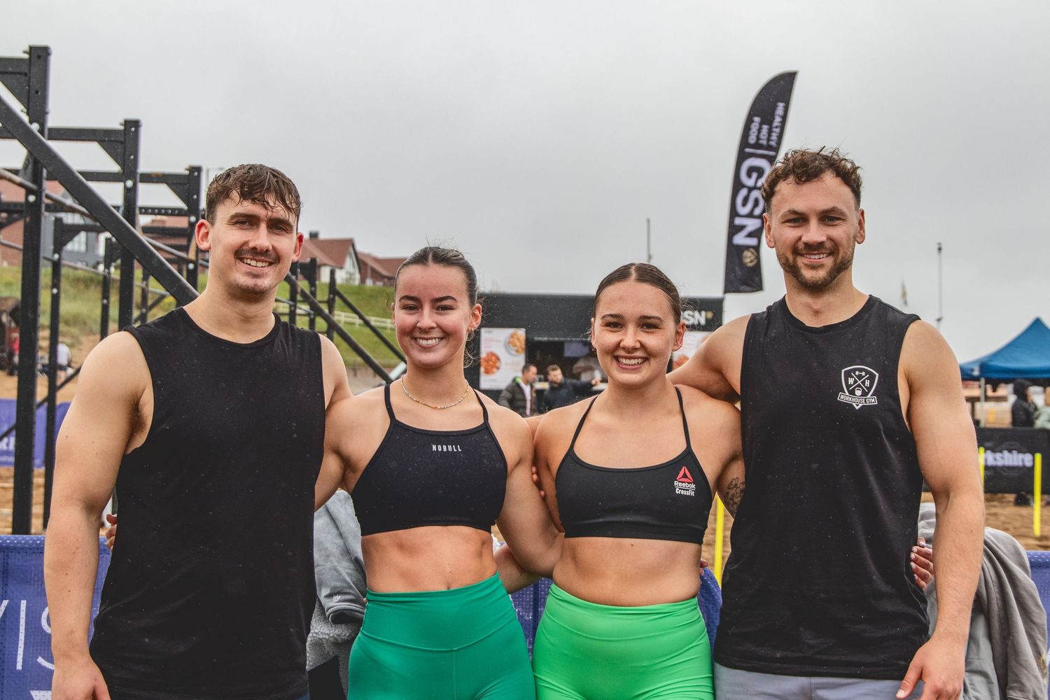 A group of four fitness enthusiasts pose together at an outdoor workout competition venue.