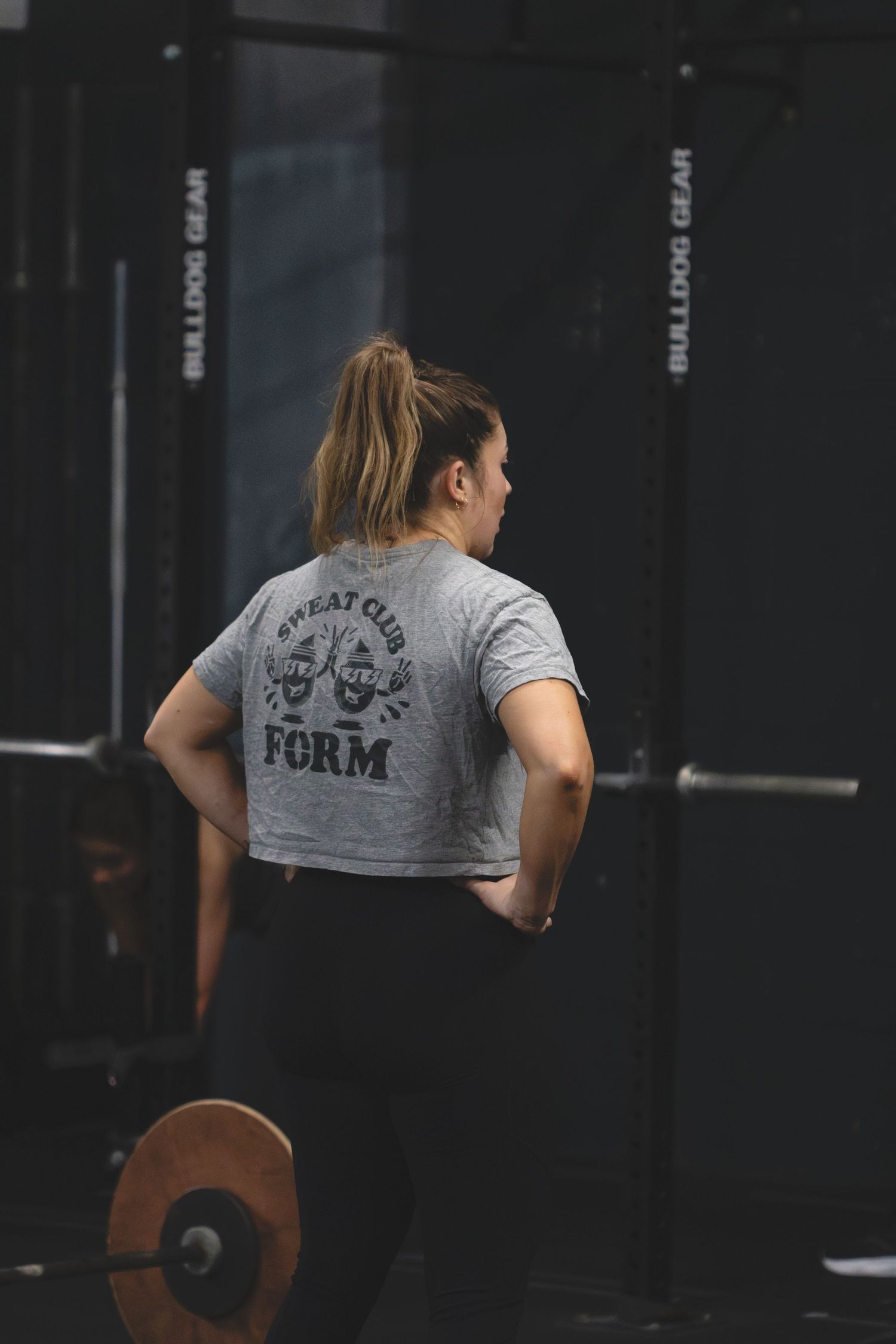 Woman in grey t-shirt lifting weights at a dark gym showing back view and determination during workout.