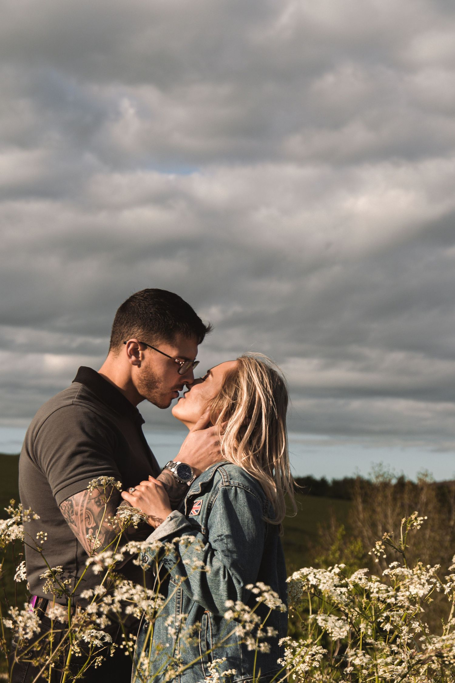 Tender moment between couple surrounded by blooming wildflowers on cloudy afternoon.