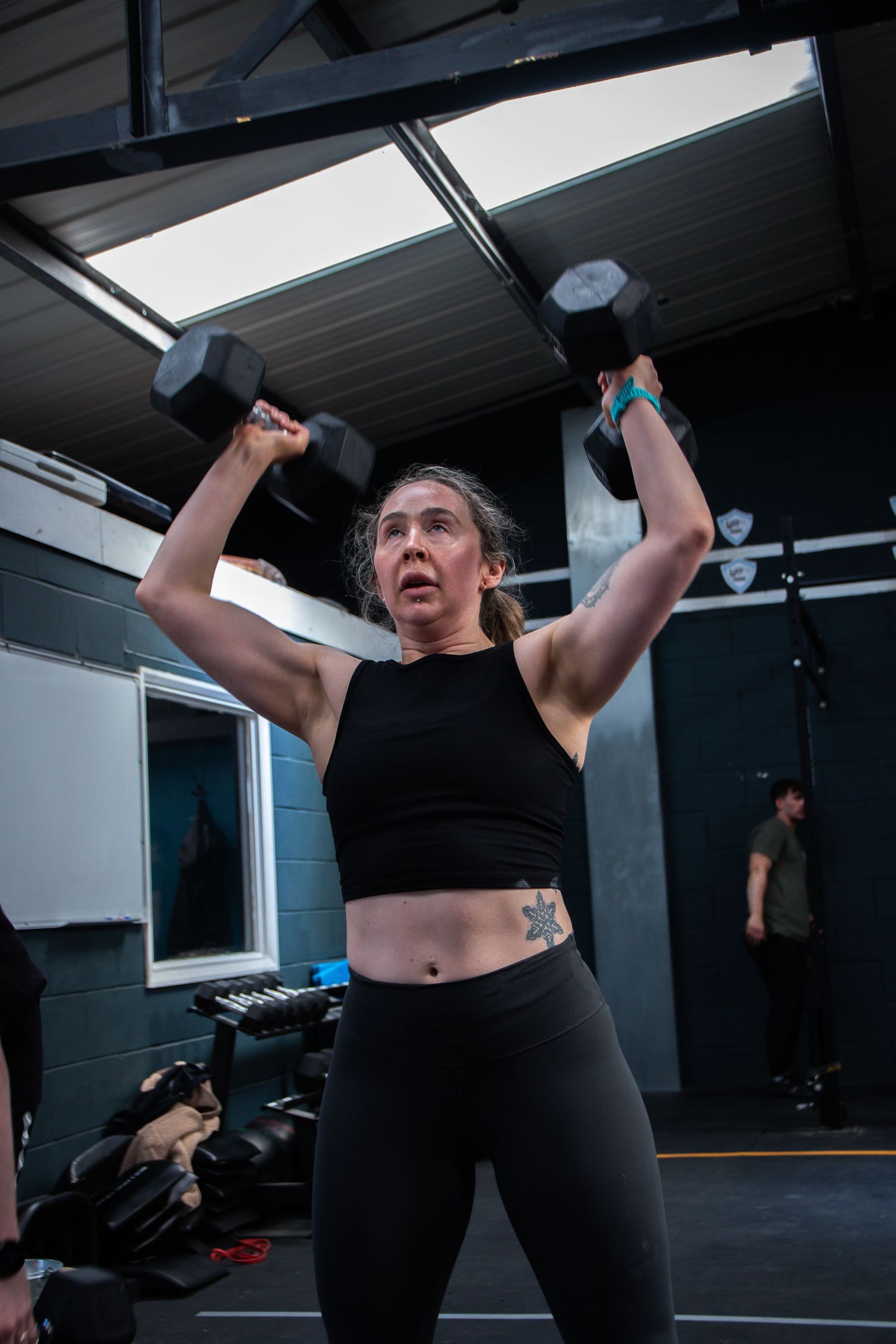 A person exercises at a gym with dumbbells, performing a sequence of overhead lifting movements in workout attire.