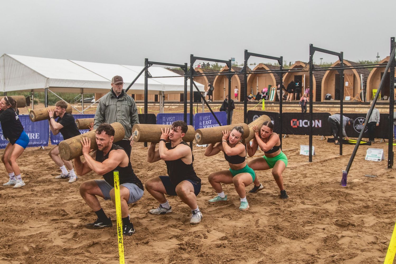 Athletes compete in a beach fitness competition performing synchronized pushups in a line formation during sunset.
