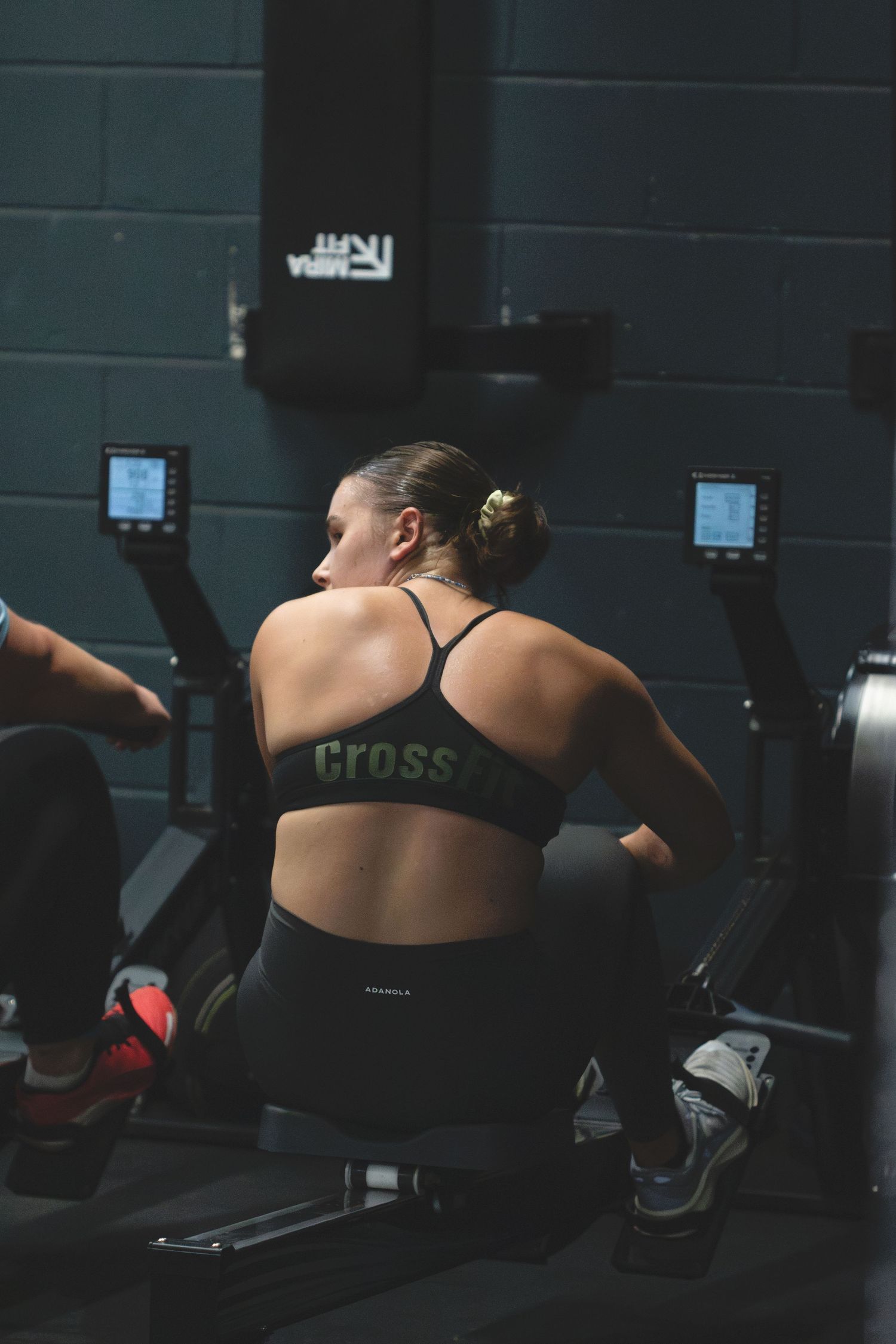 Athletic person in black sportswear working out on rowing machine at CrossFit gym during intense training session.