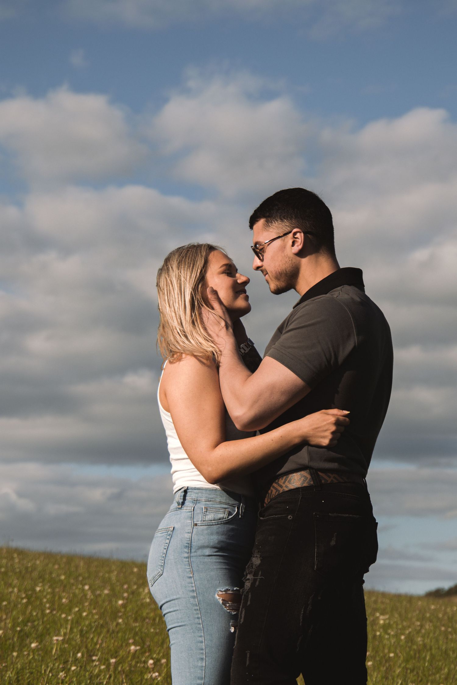 Romantic capture of a couple sharing an embrace against a dramatic cloudy sky in a meadow.