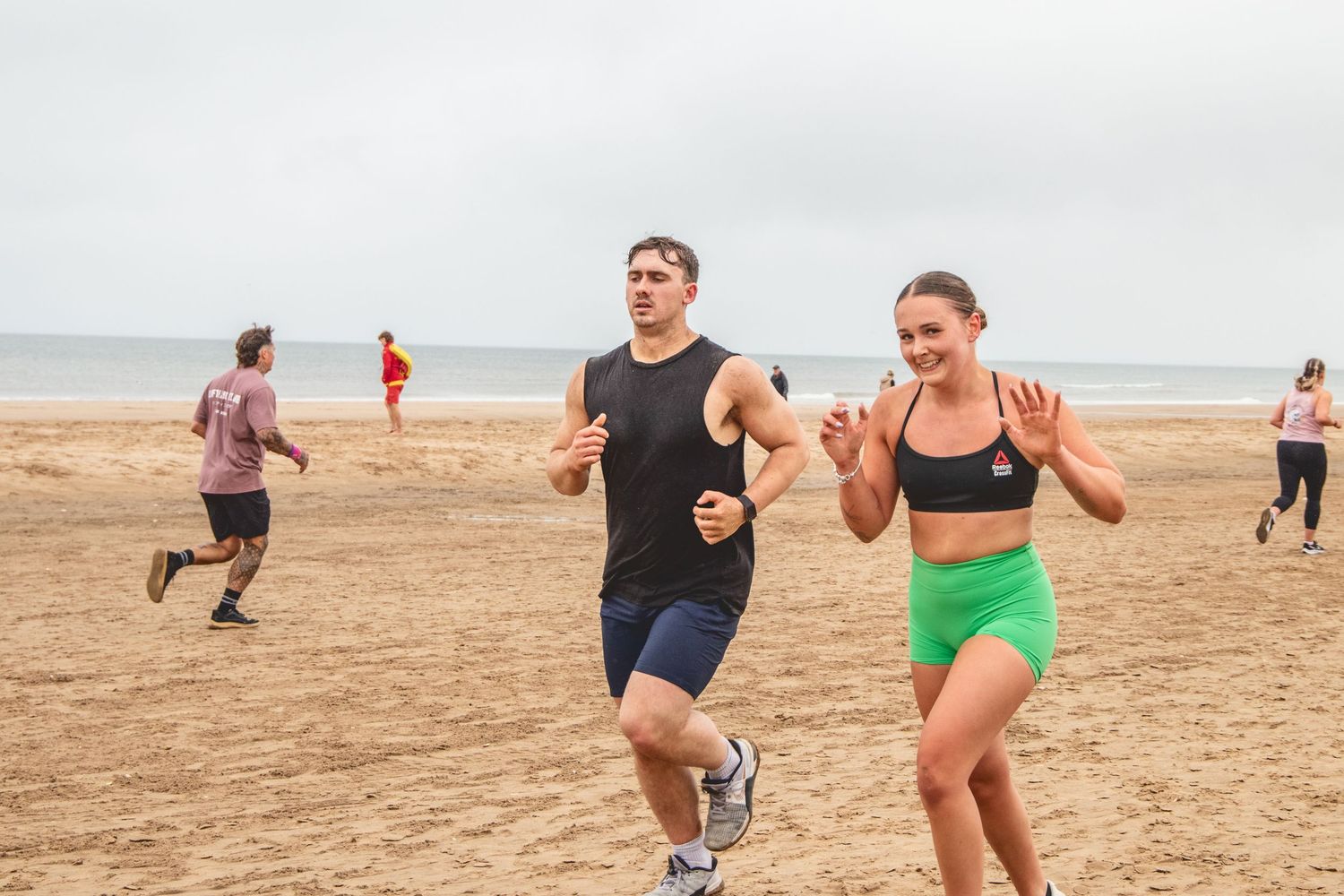 Group of runners exercising together on a sandy beach during a cloudy day.