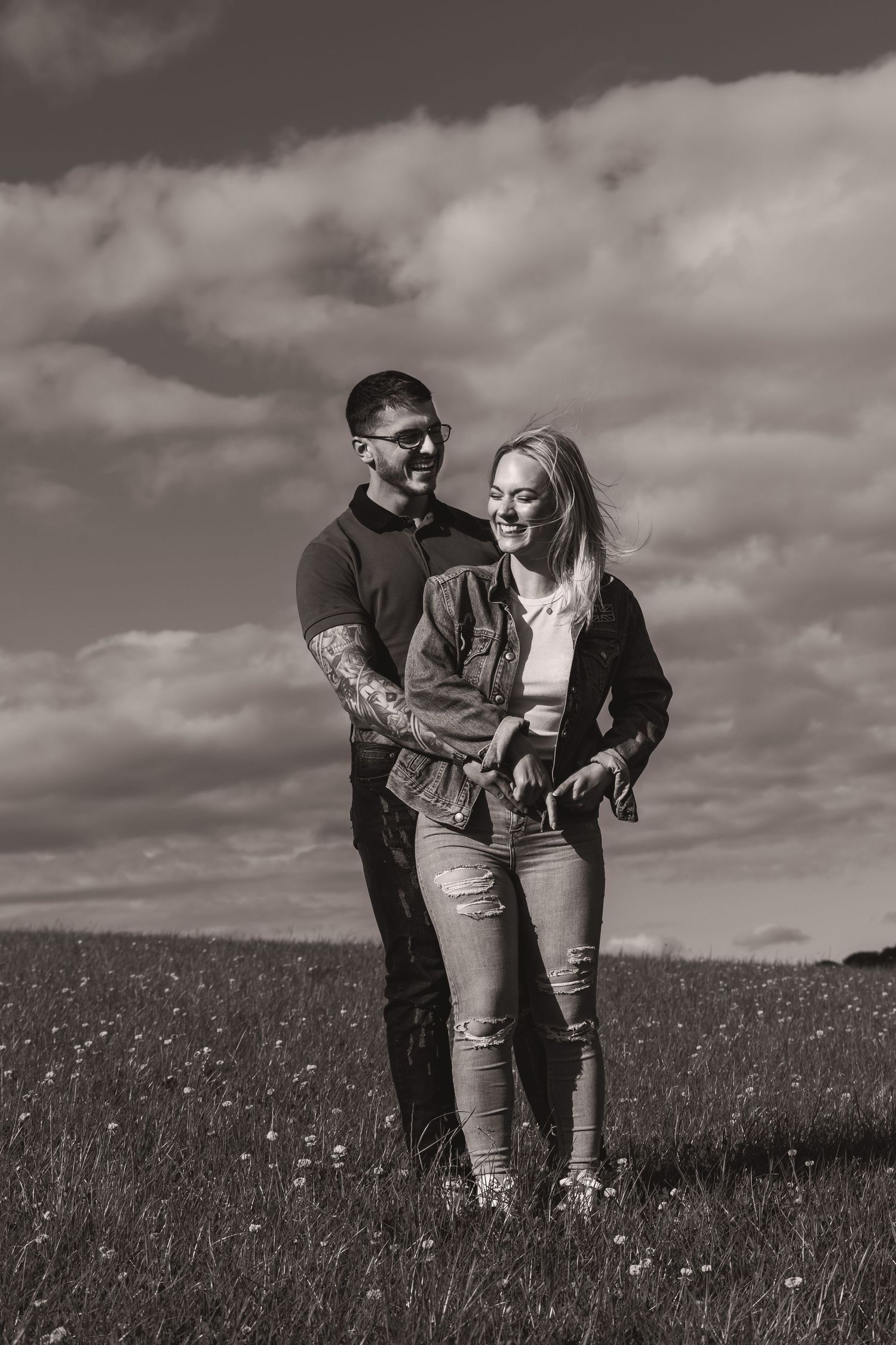 Couple standing together in a wildflower meadow under dramatic clouds.