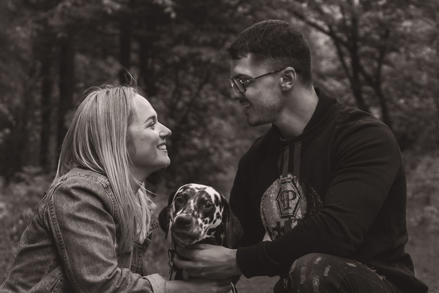 Intimate black and white portrait of a couple with their Dalmatian in a forest setting.