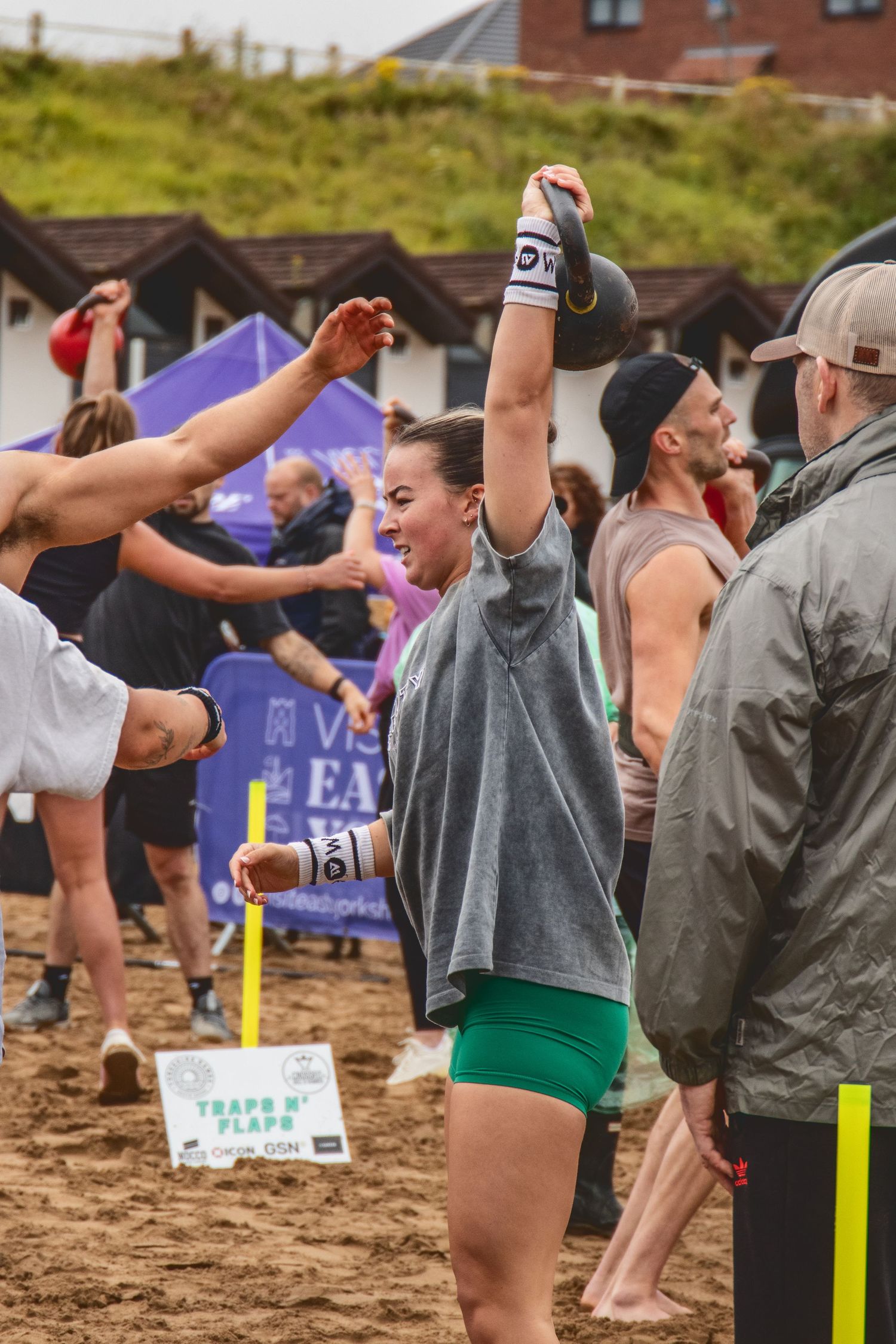 Athlete celebrates enthusiastically during outdoor beach fitness competition with crowd and sand in background.