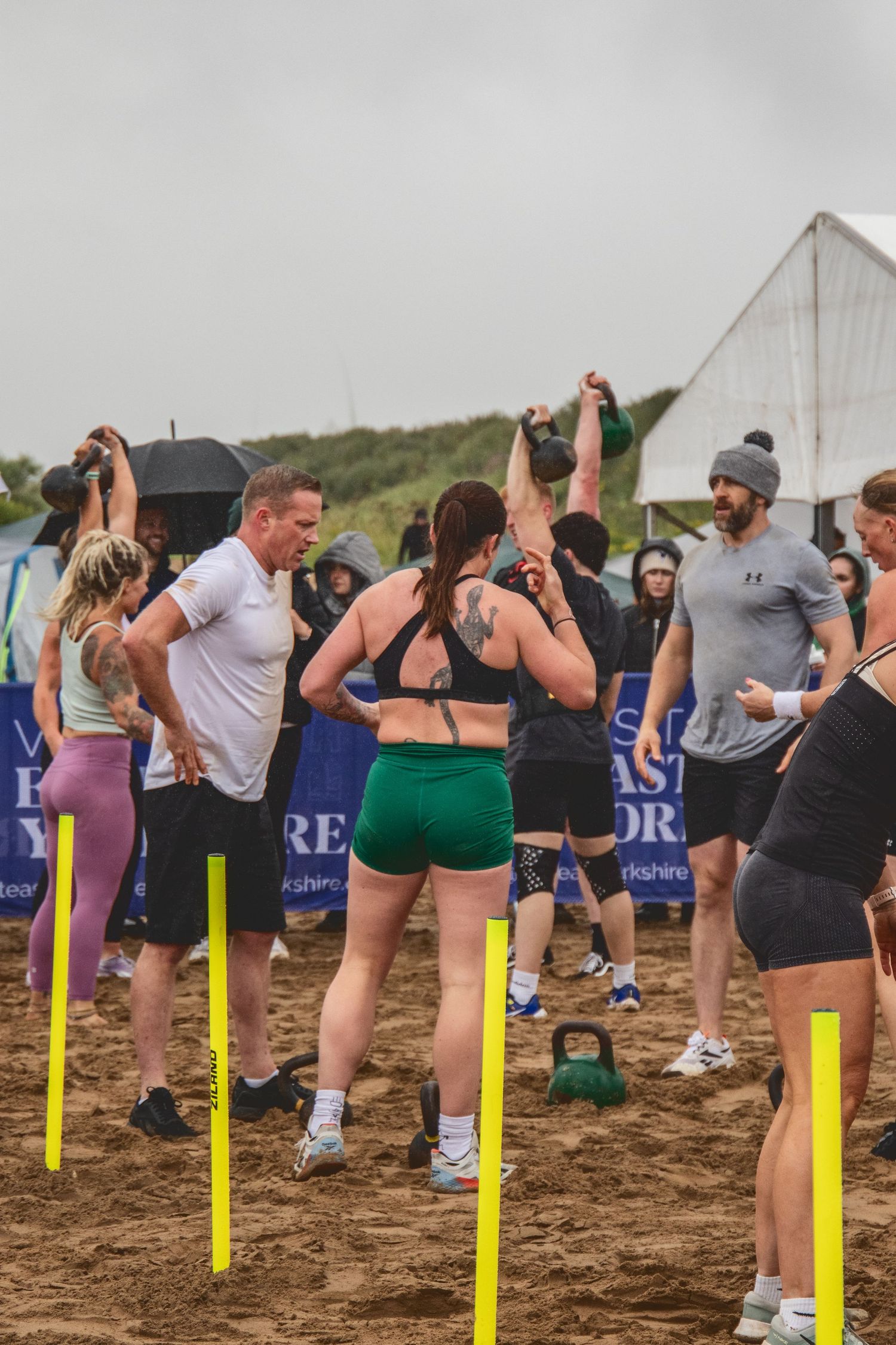 Fitness participants gather around yellow markers during an outdoor group training session on muddy ground.