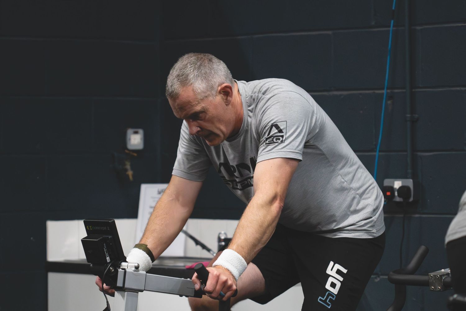 A person performs a workout with weights on a barbell in a dark gym setting with black walls.