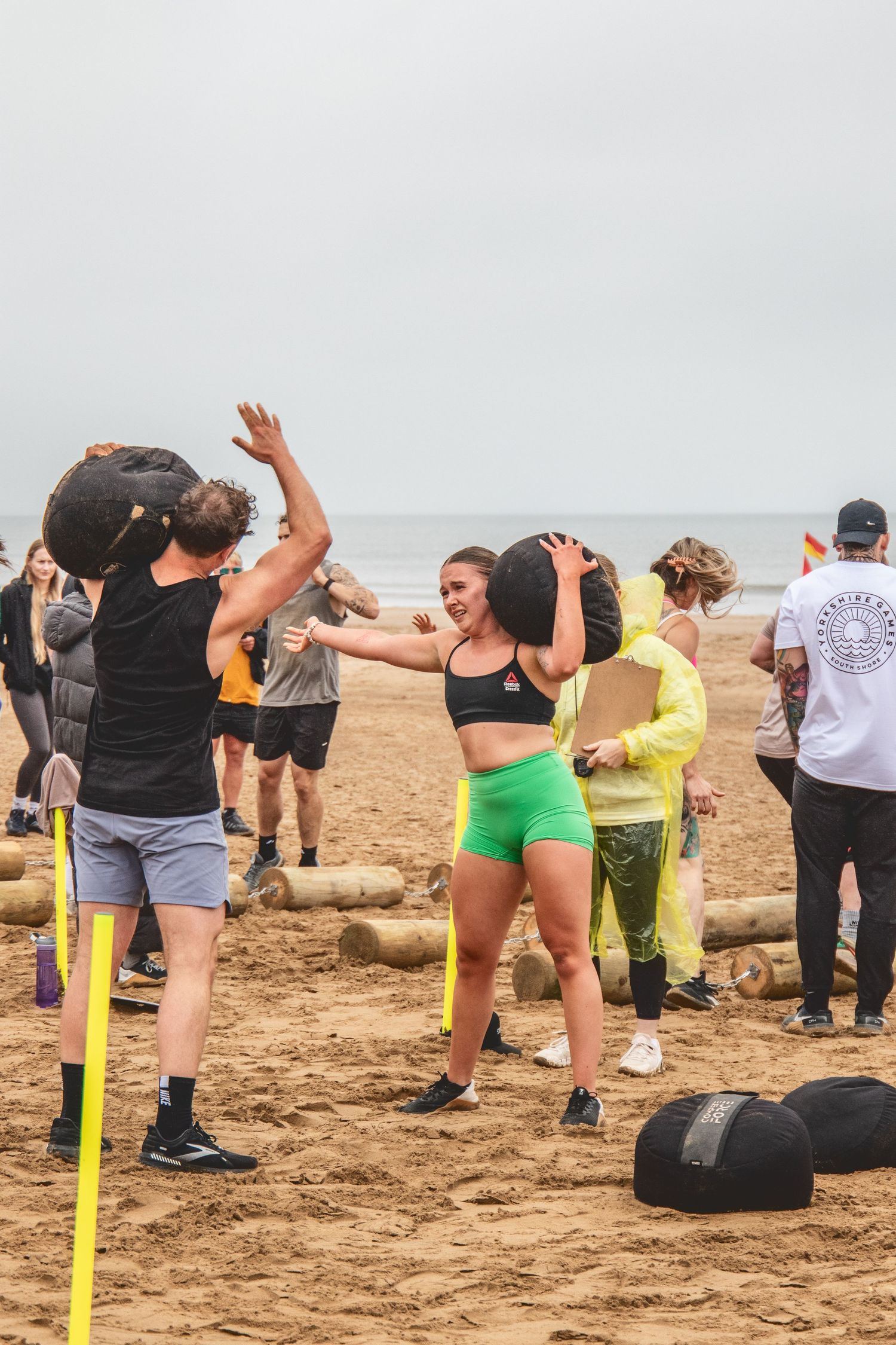 Group exercising with resistance bands on a sandy beach with driftwood scattered around during an outdoor fitness class.