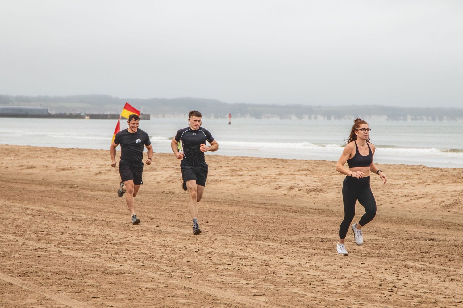 People running during an outdoor exercise session along a sandy beach near the ocean.