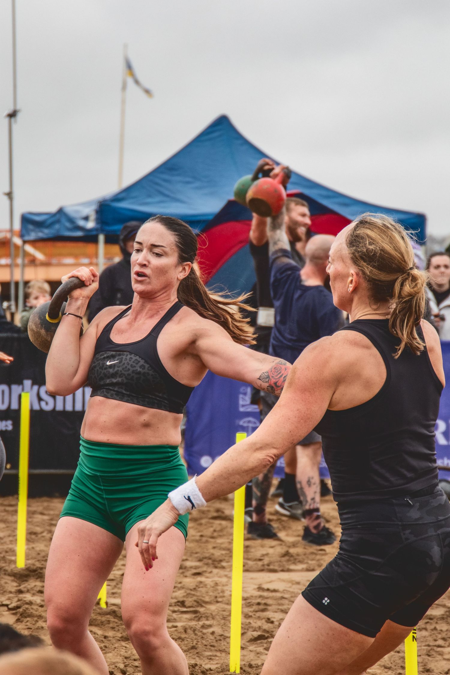 Athletes compete during an outdoor CrossFit competition with tents and flags visible in the background.