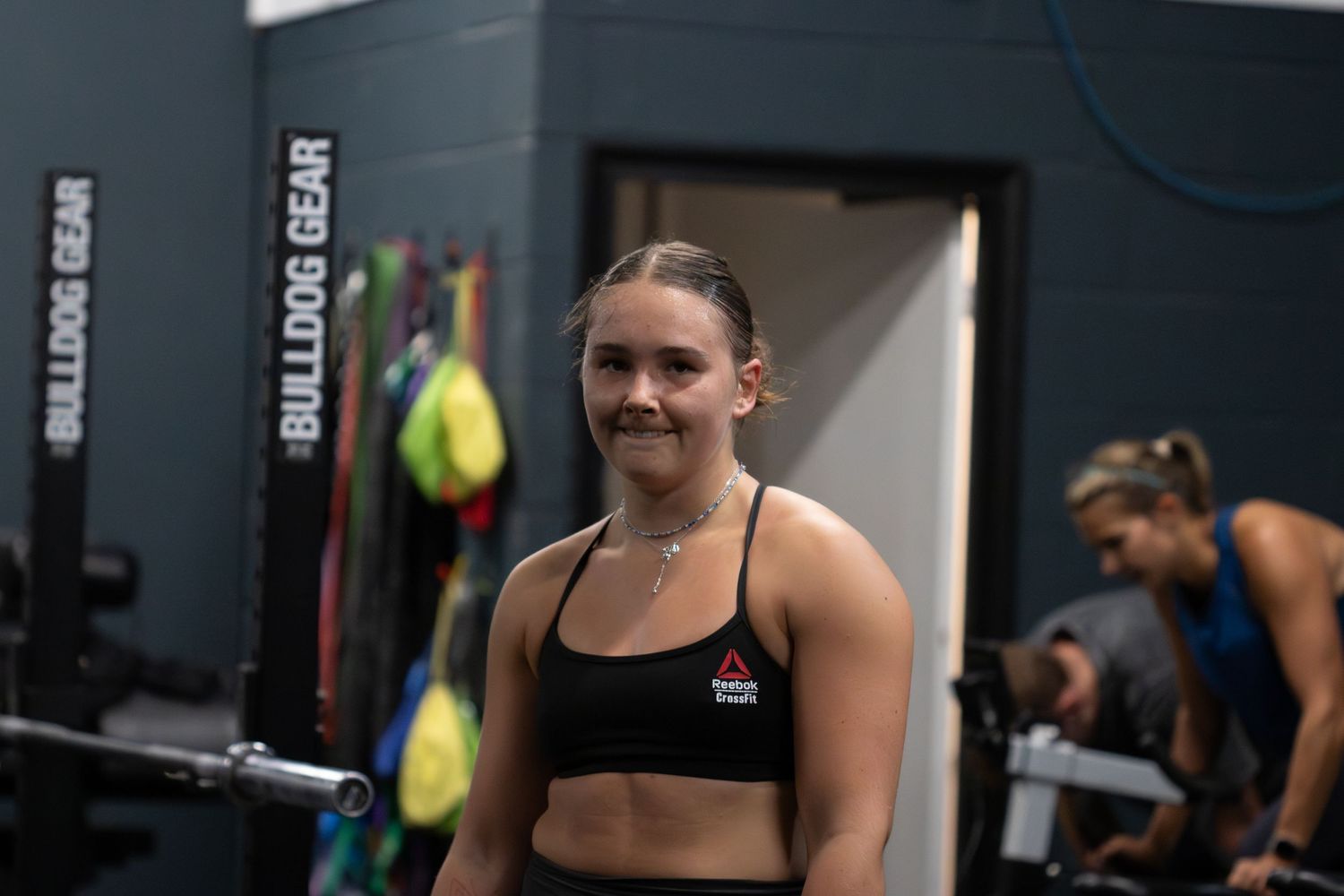 CrossFit athletes perform a weightlifting exercise inside a well-equipped gym with barbells and fitness equipment.